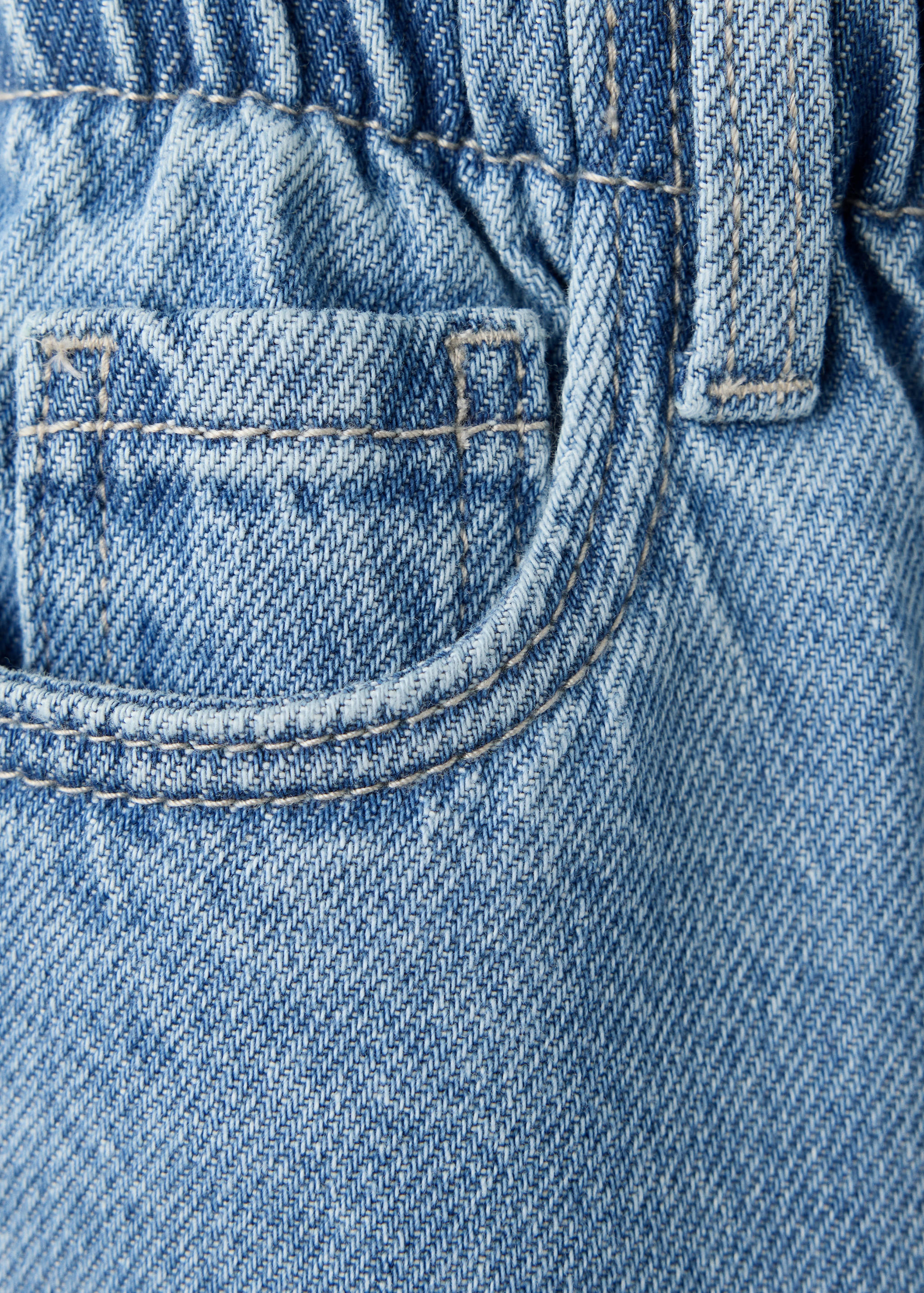 Close-up of light blue denim trousers with an elastic waistband and coin pocket.
