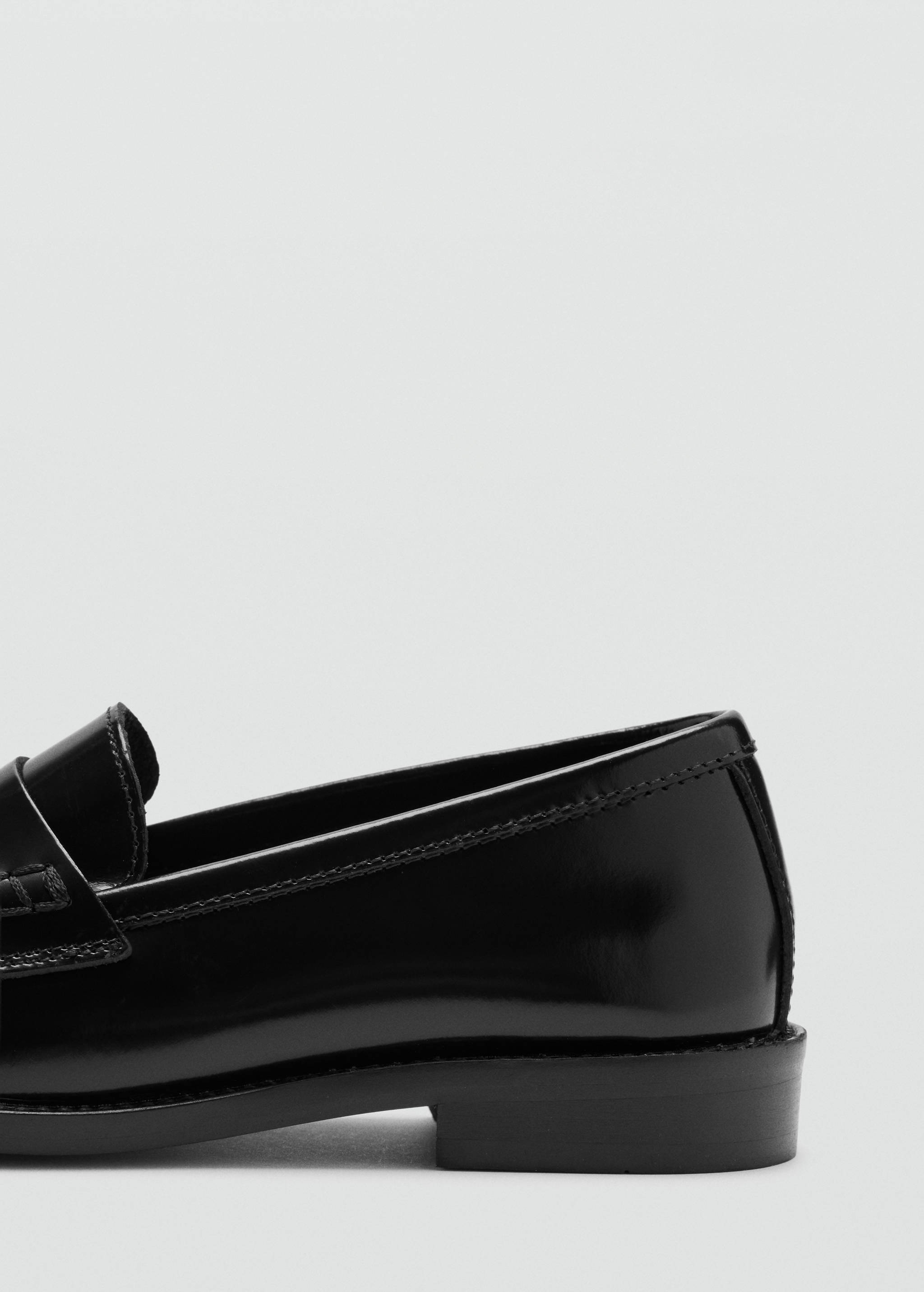 Close-up of a black patent leather loafer showing the side profile and penny strap.