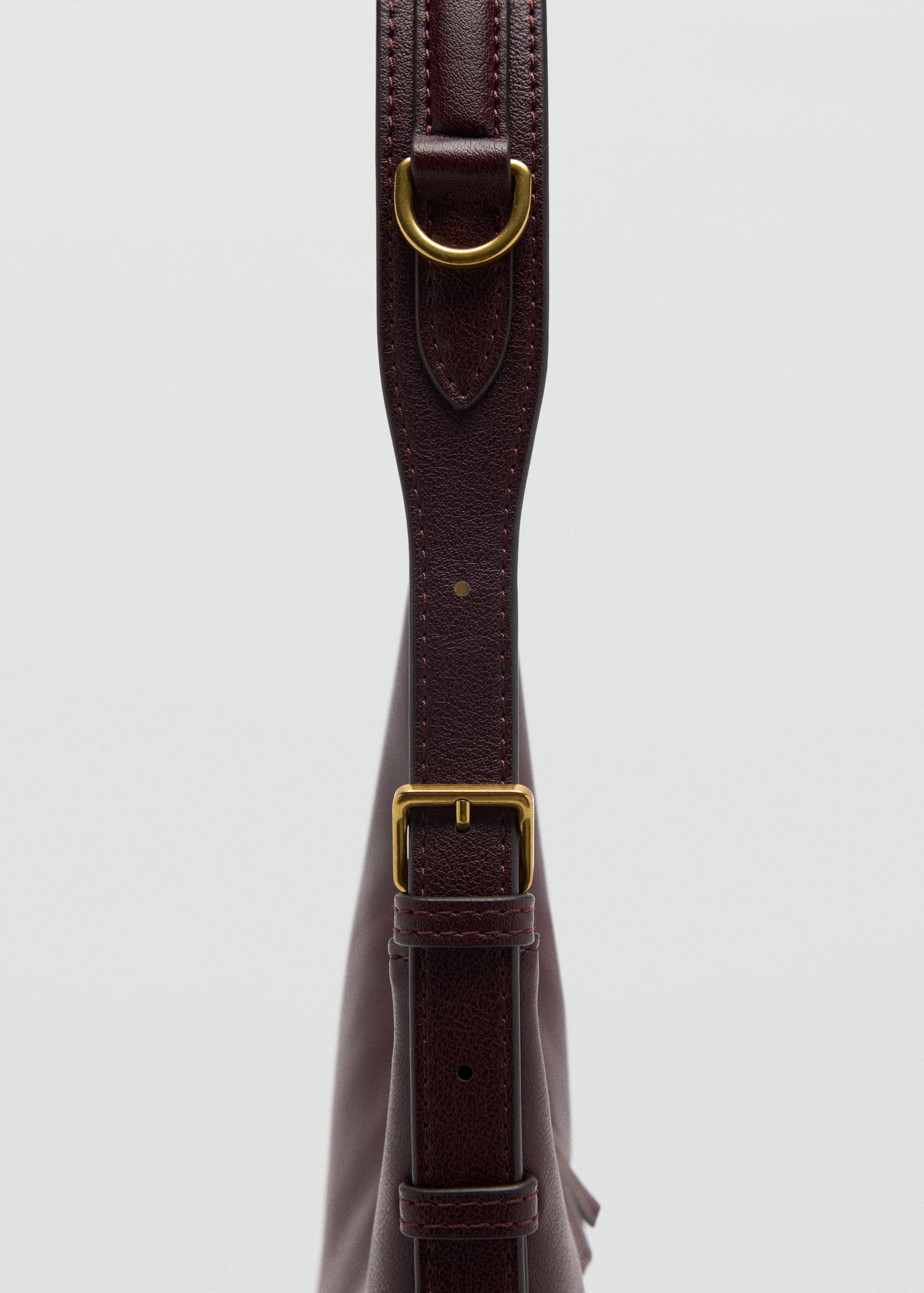 Detalle de asa de bolso shoulder burdeos con herrajes metálicos en tono latón.