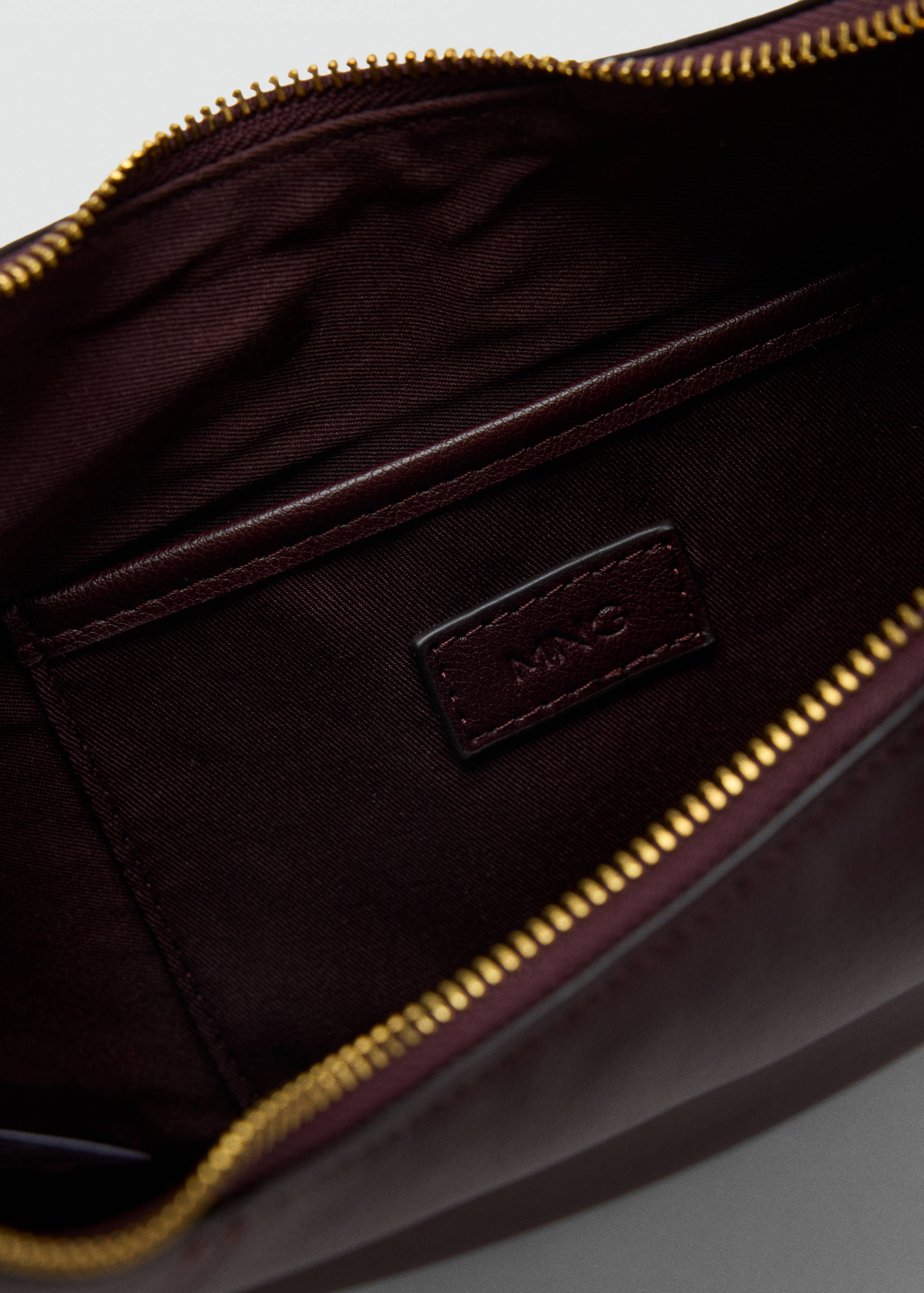Detalle del interior del bolso shoulder burdeos que muestra el forro y la etiqueta con el logotipo.