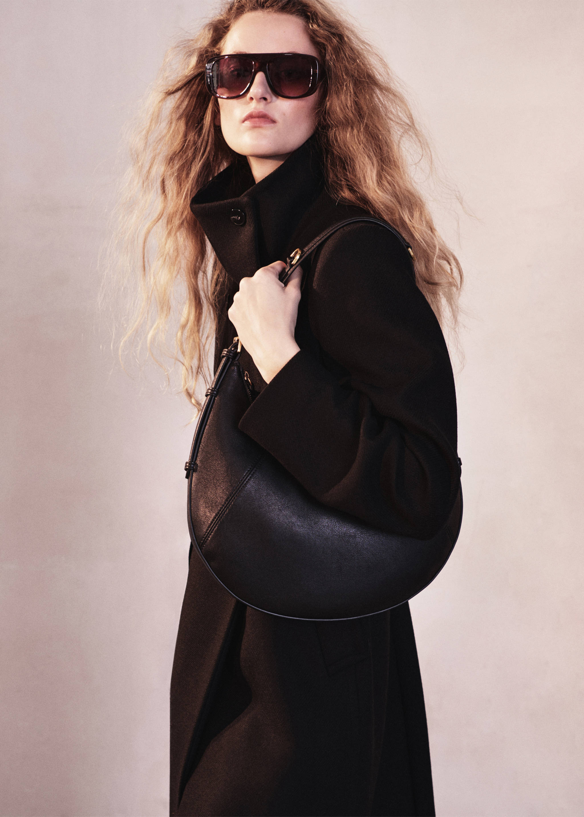 Bolso de hombro de piel en color negro con ribetes estructurados y detalles metálicos dorados.