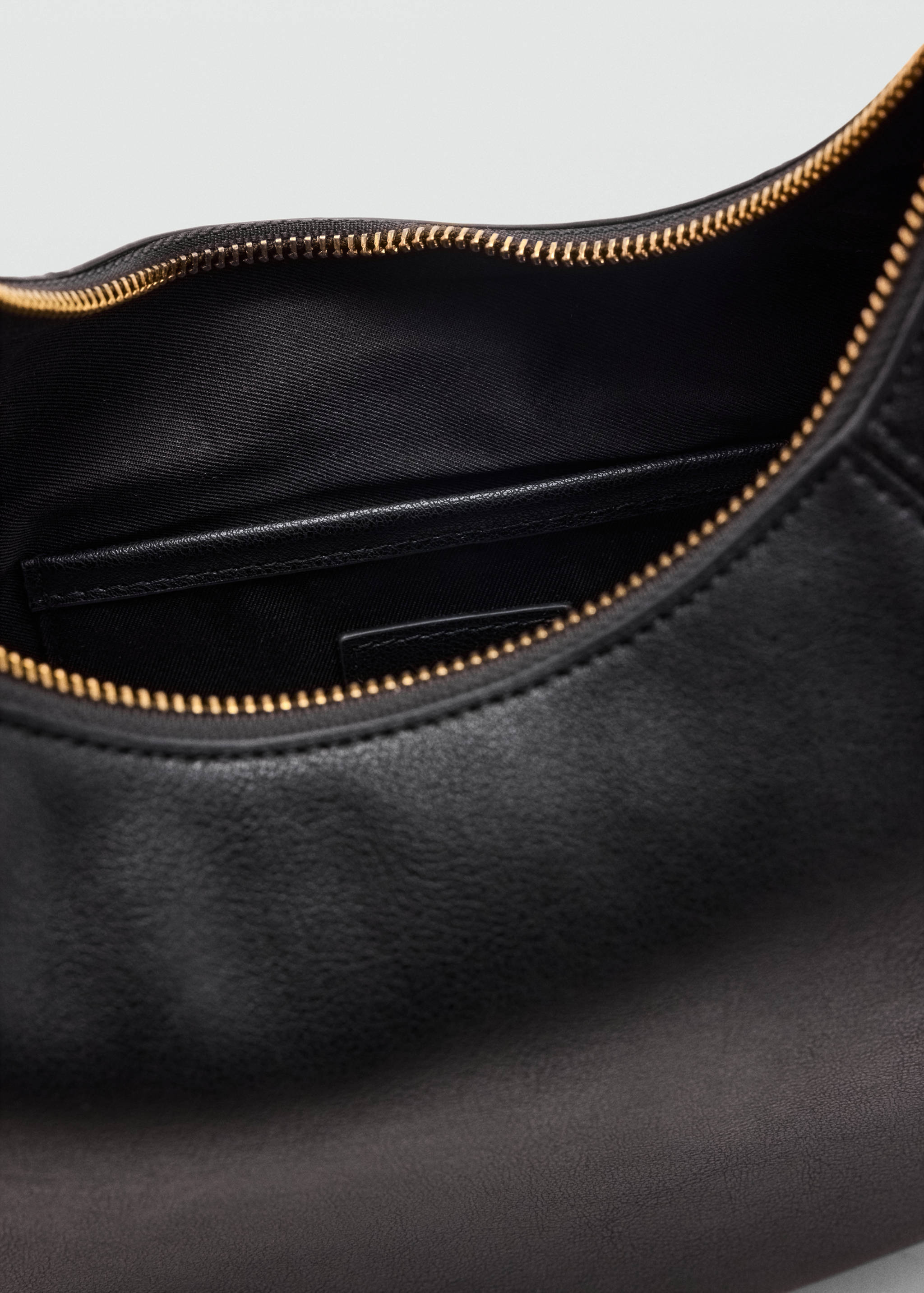 Primer plano del interior de un bolso shoulder negro con cierre de cremallera.