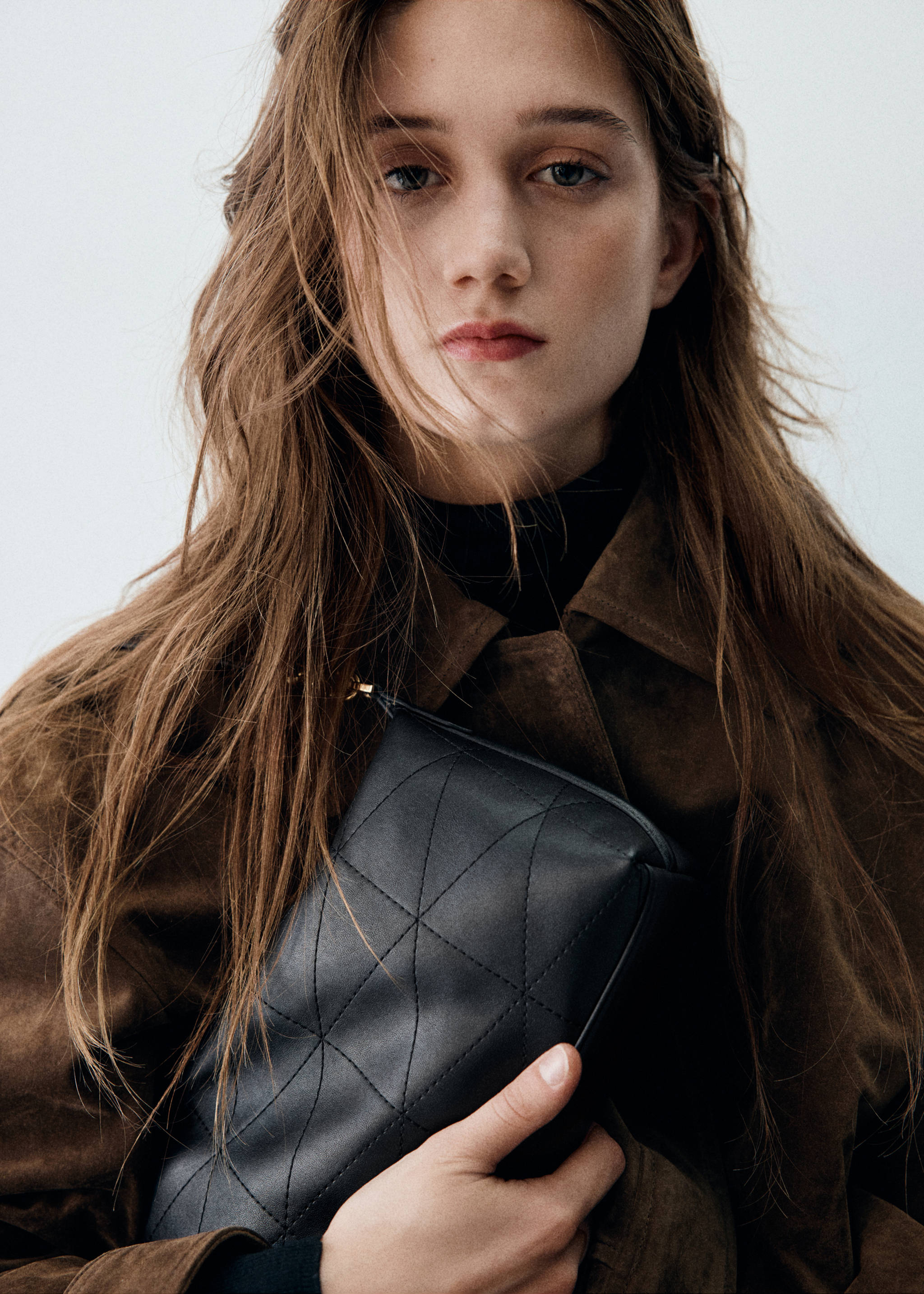 Bolso bandolera acolchado en color negro con pespuntes geométricos, sujeto por una modelo.