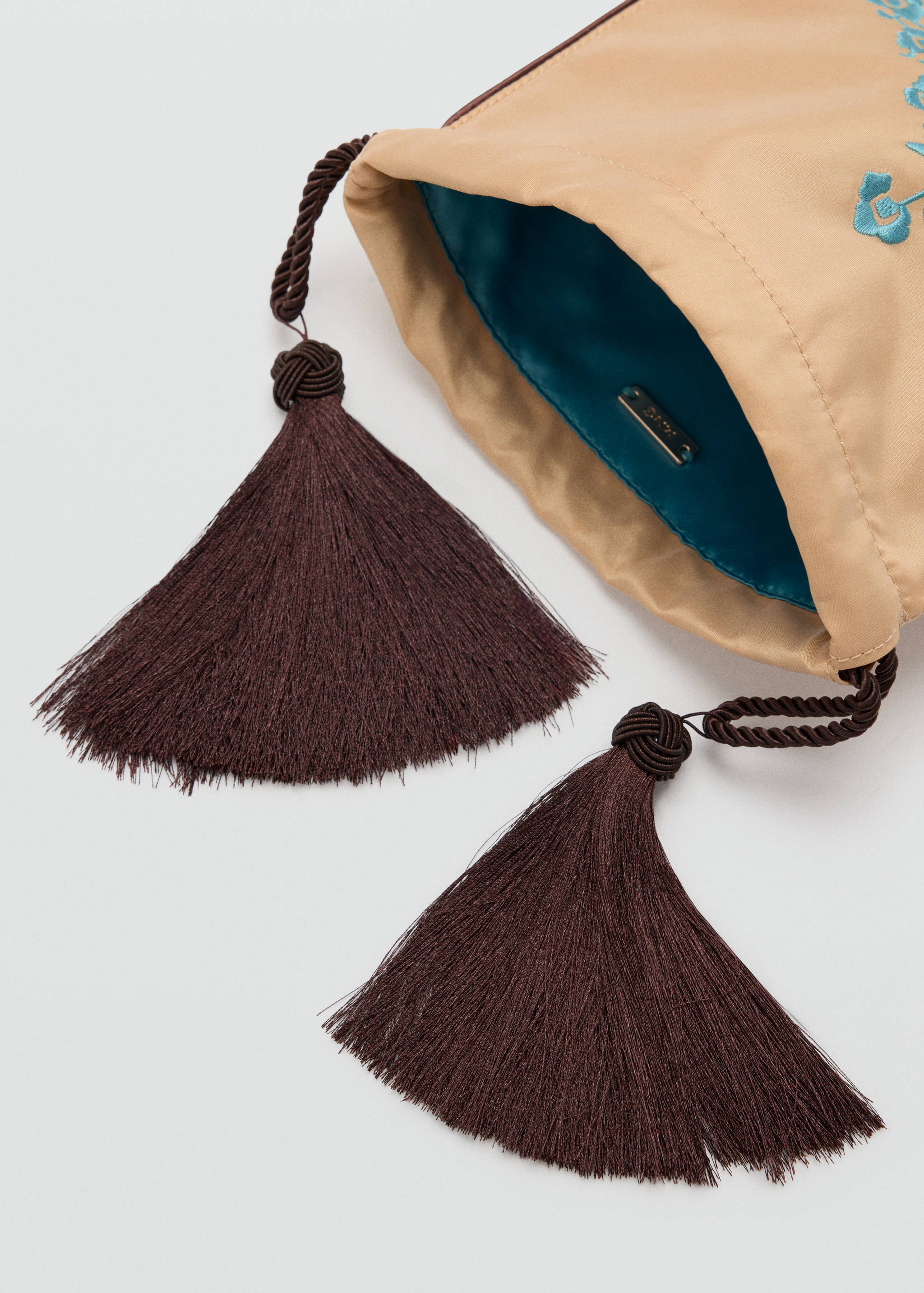 Close-up of a beige handbag with large dark brown tassels.