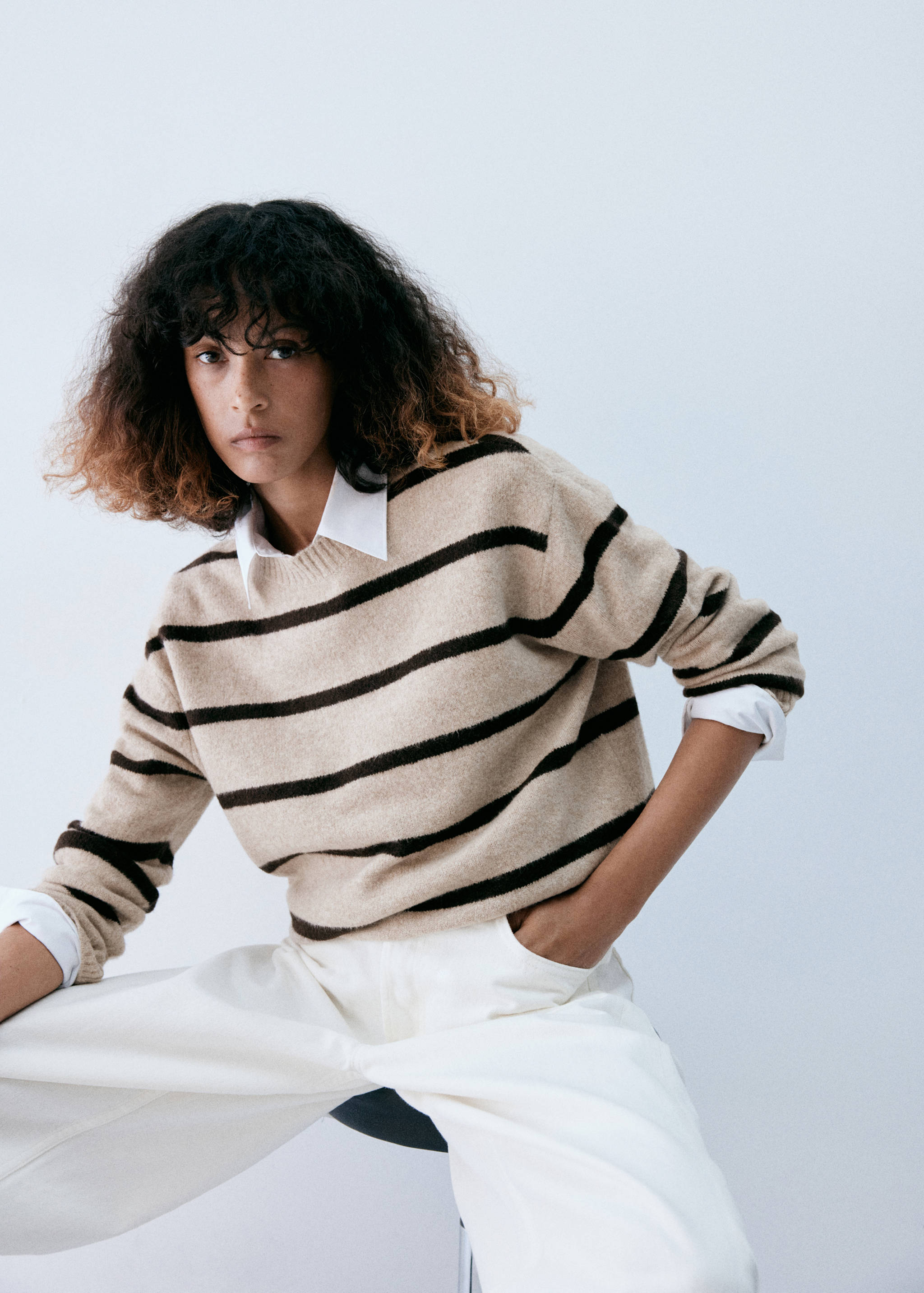 Beige striped knit jumper with a round neckline over a white shirt.