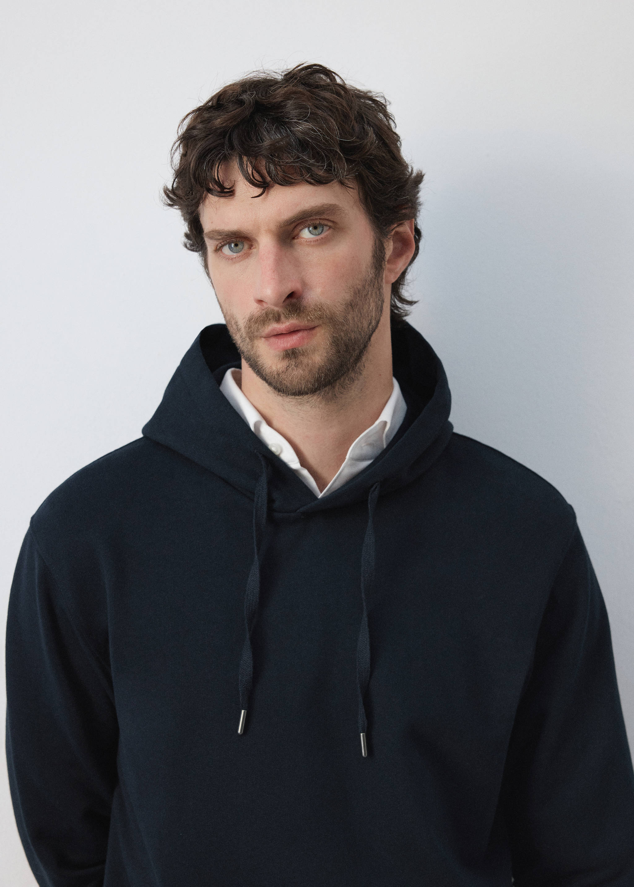 Navy blue hooded sweatshirt with drawstrings, worn over a white collared shirt.