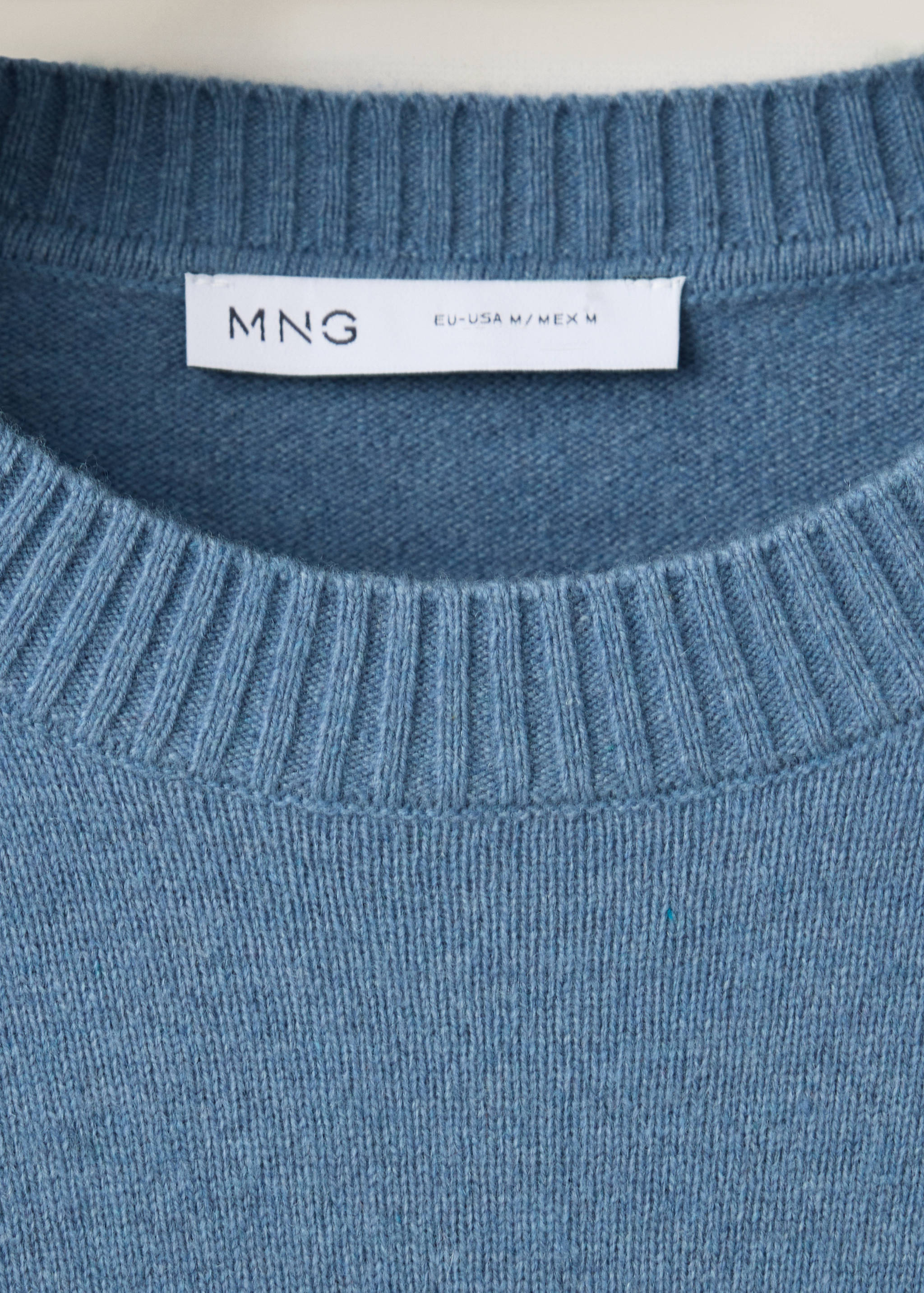 Detalle de jersey de punto azul con cuello redondo canalado.