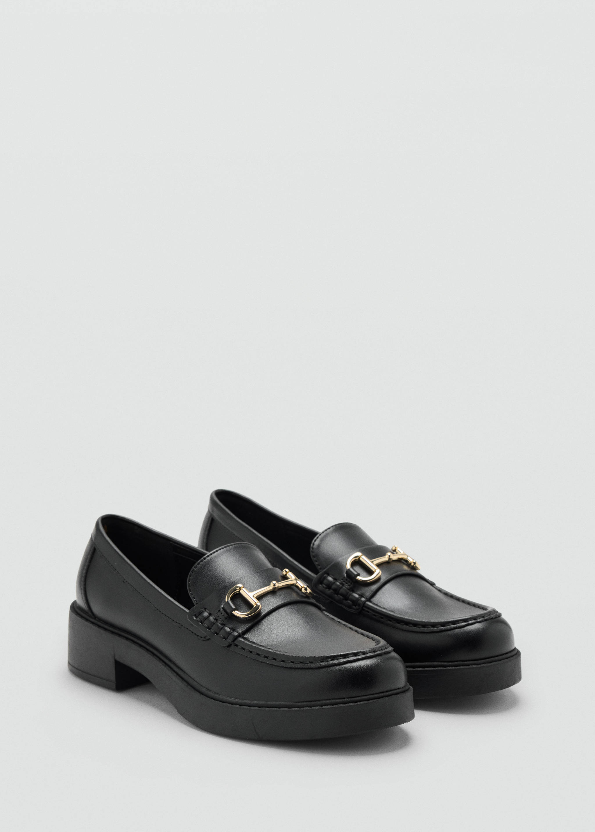 Mocasines negros con suela de plataforma y detalle de estribo en tono dorado.