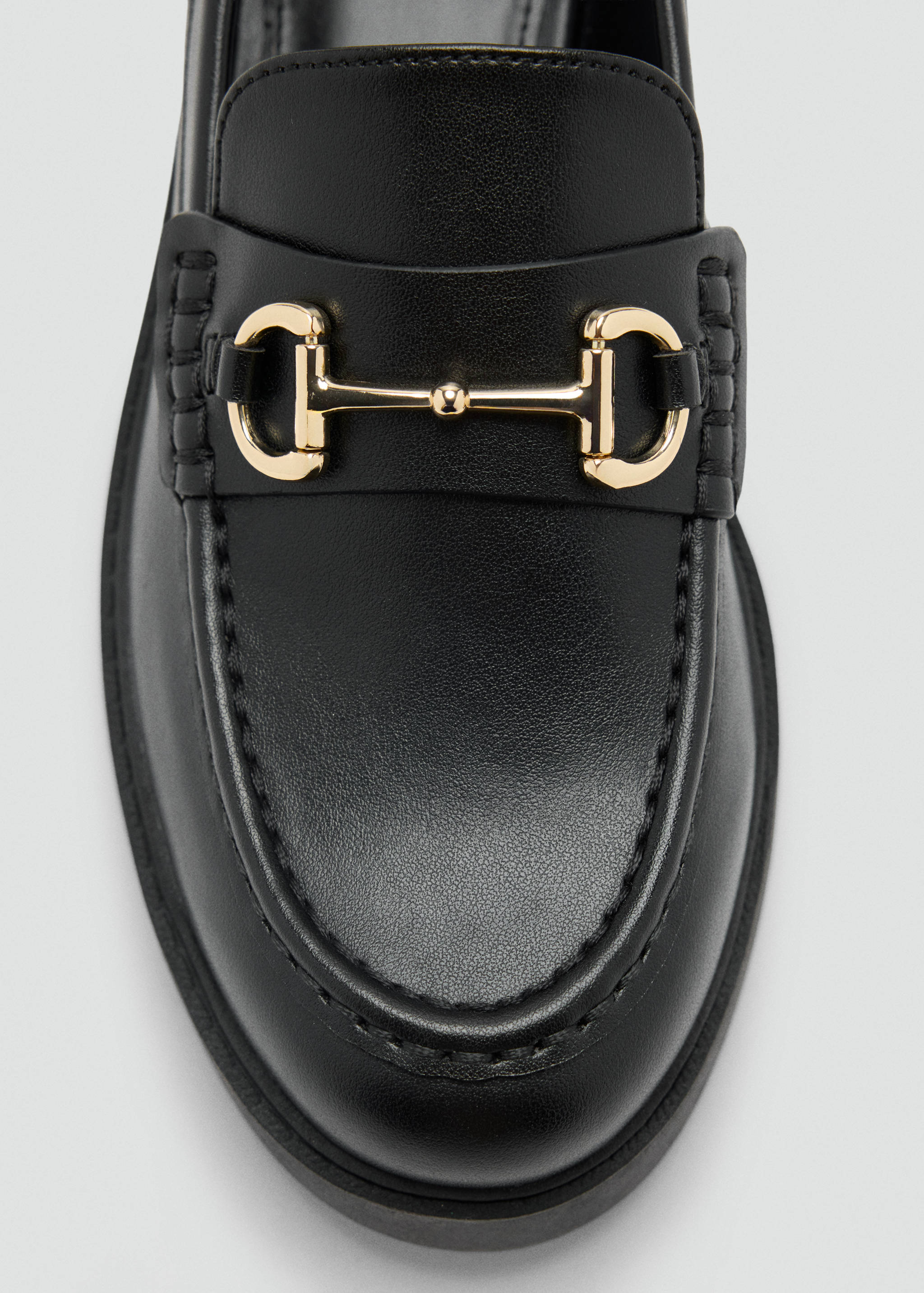 Primer plano de un mocasín negro con detalle de hebilla metálica dorada.