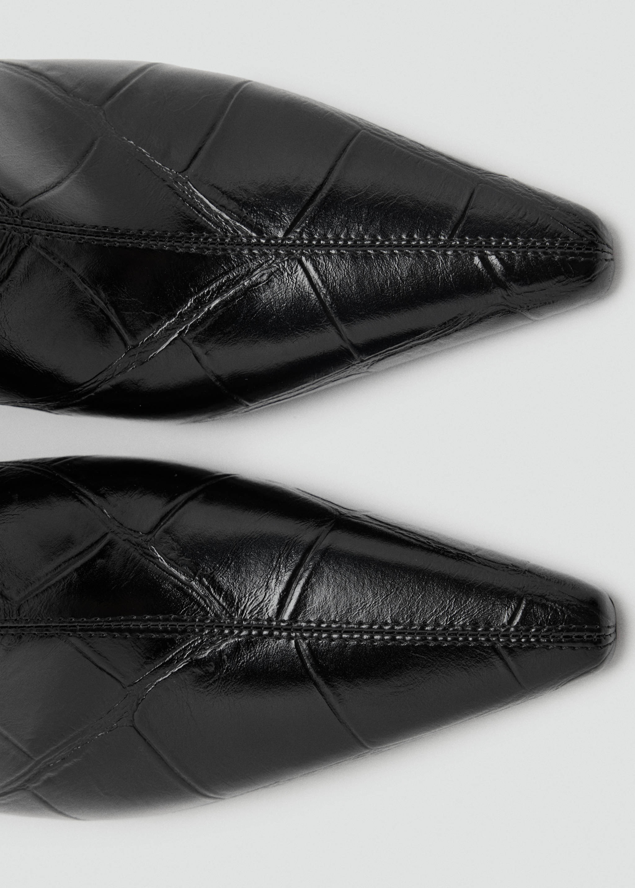 Close-up of black glossy crocodile-embossed pointed ankle boots.