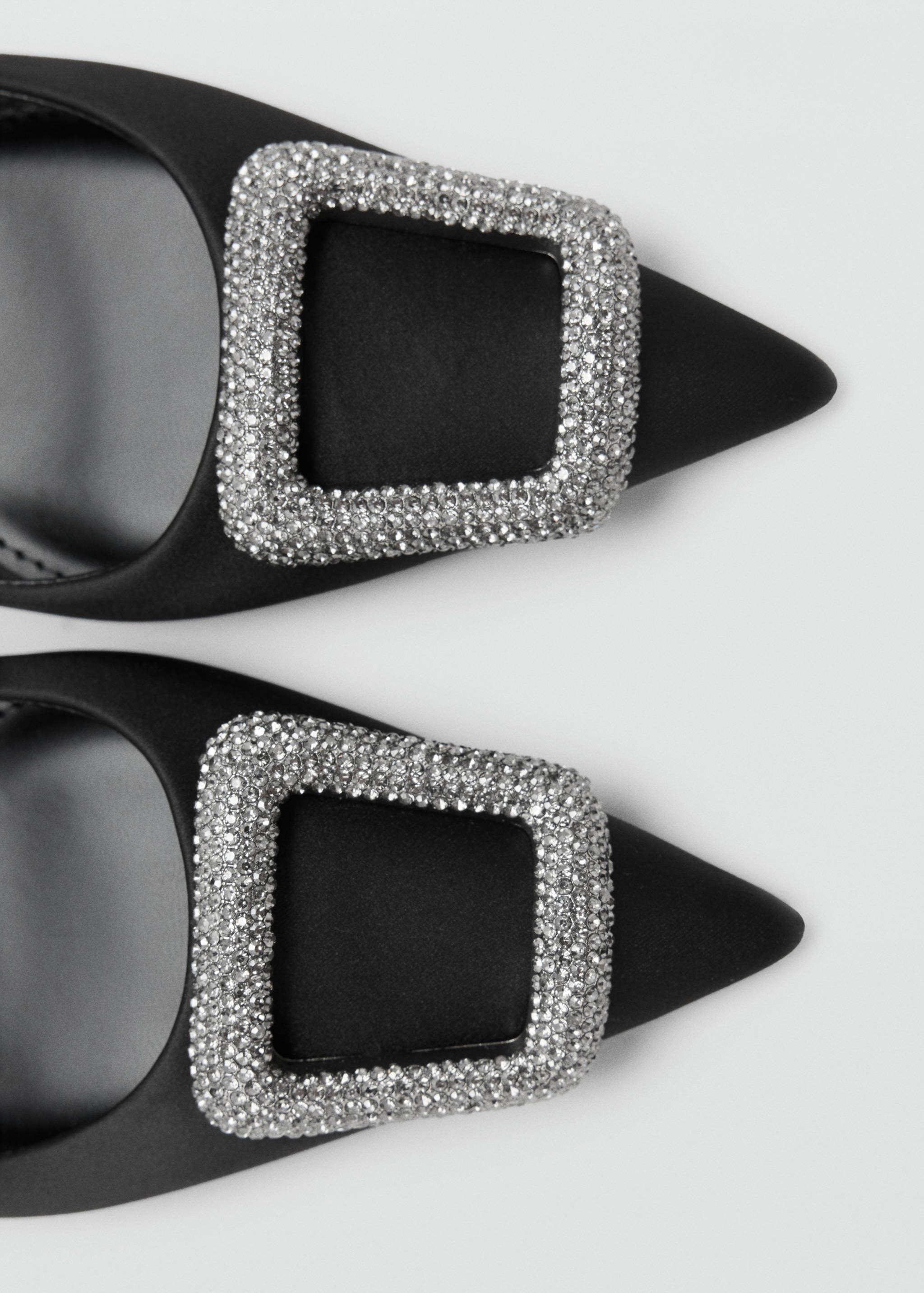 Close-up of black satin shoes with crystal buckle detail.