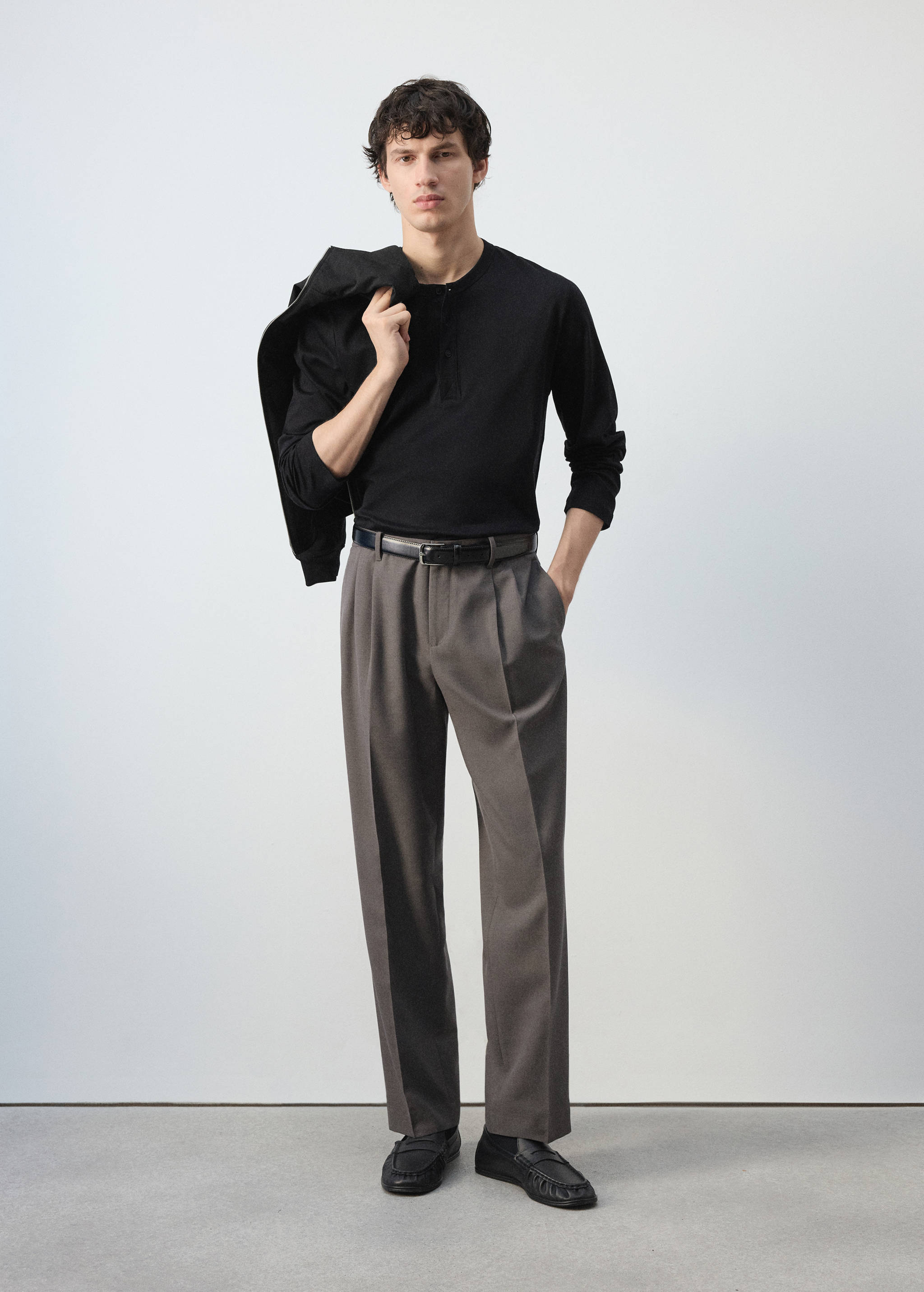 Grey pleated trousers worn with a black long-sleeved top and belt