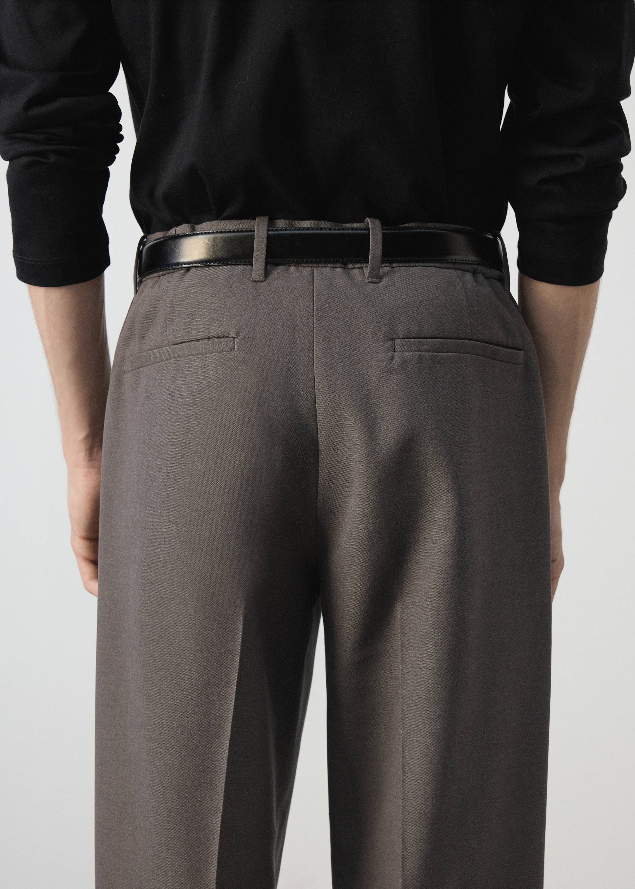 Back view of grey trousers with a black belt, worn with a black top.