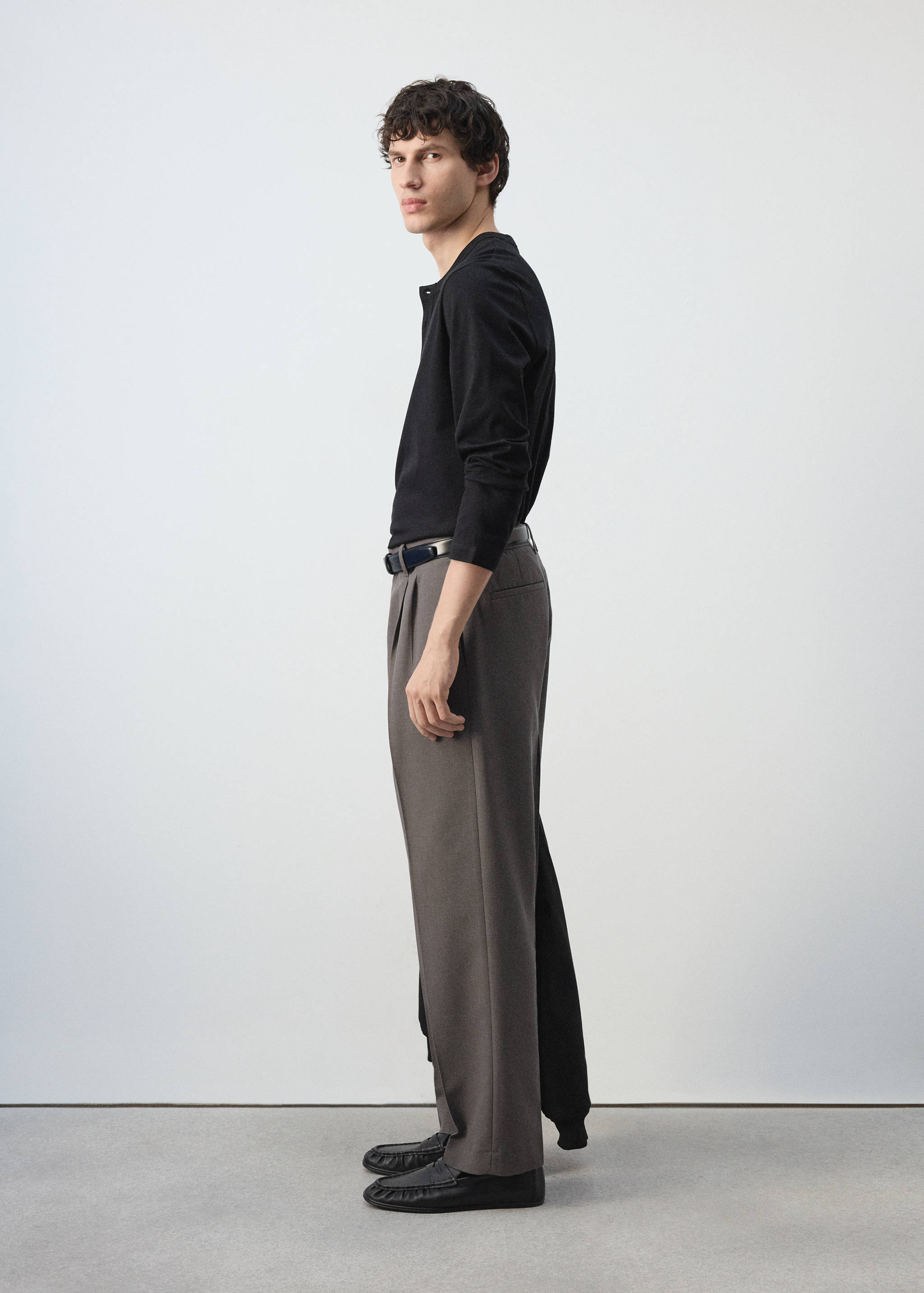 Grey pleated trousers worn with a black long-sleeved polo and shoes.