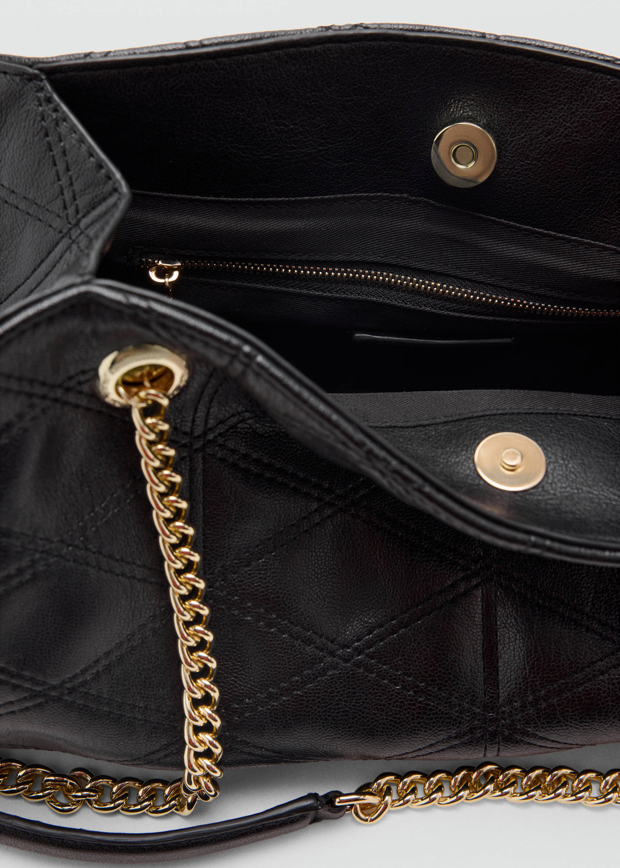 Detail of a black quilted shoulder bag with gold chain strap and magnetic snap closure.