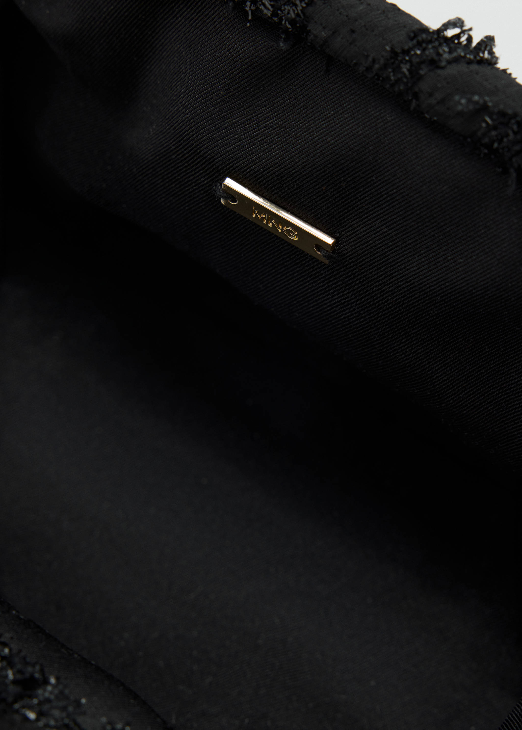 Close-up of a black handbag interior with a gold MNG brand plaque.