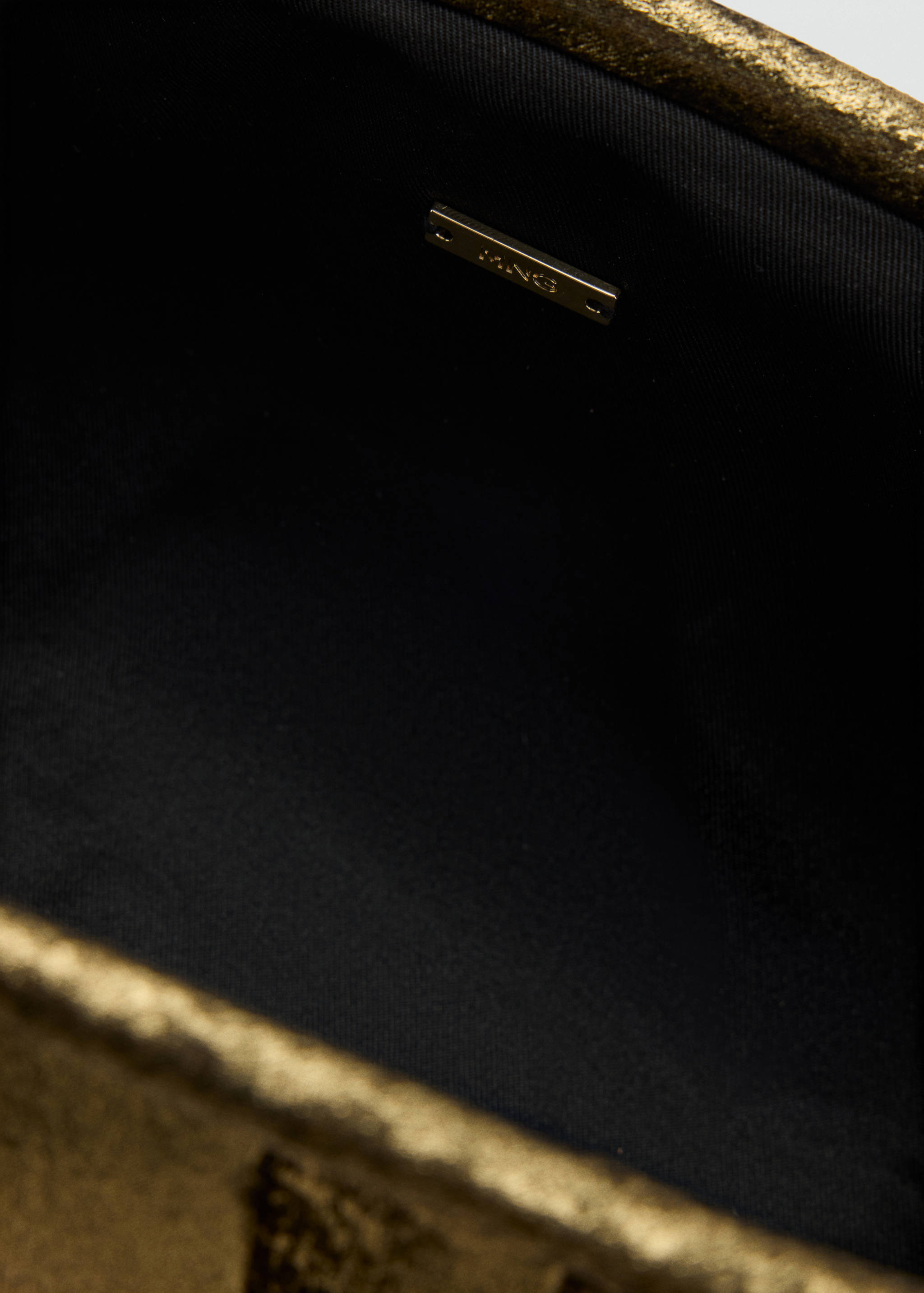 Close-up interior of a metallic gold handbag showing the brand plaque.