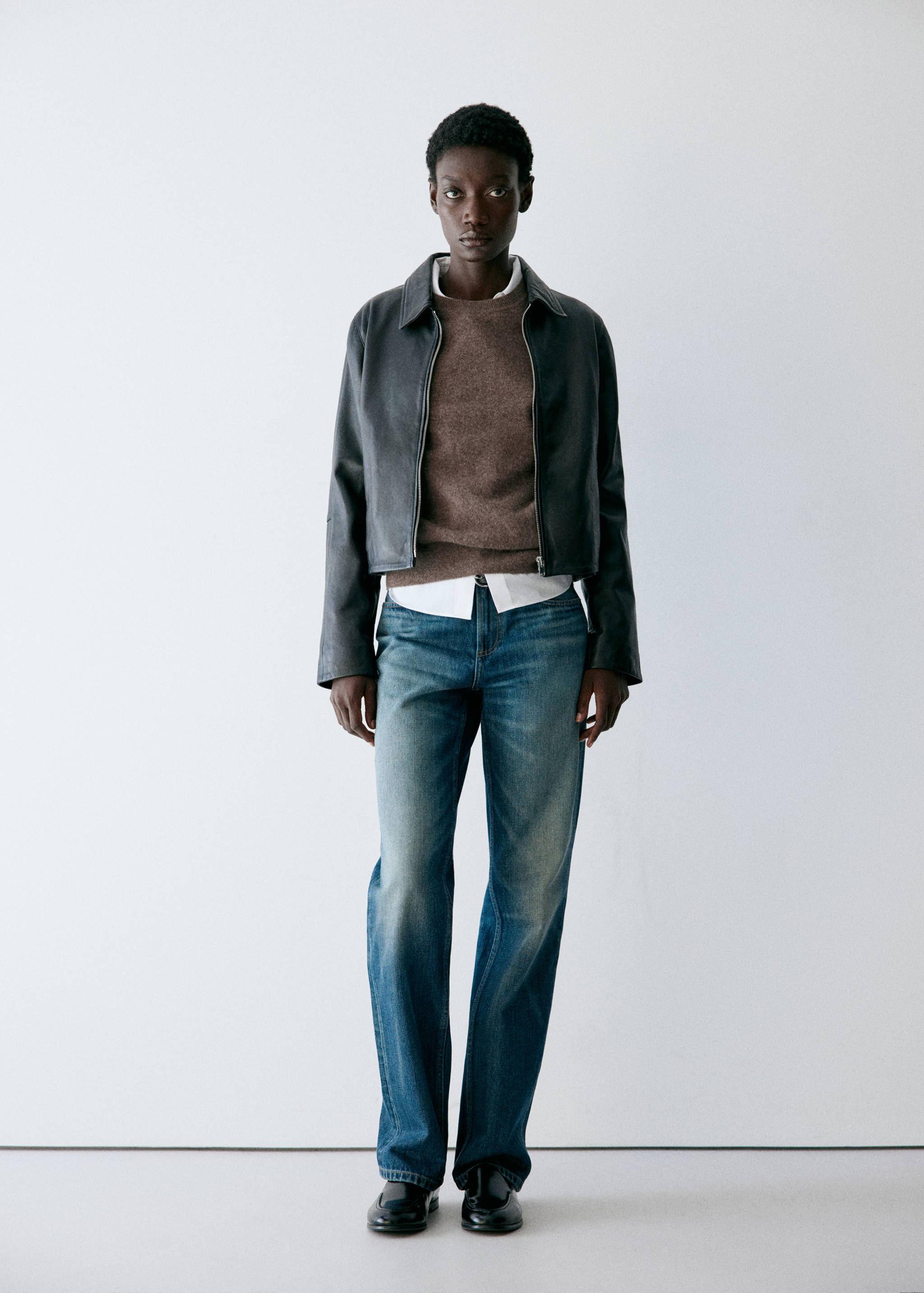 Brown knit jersey layered with a white shirt, styled with a leather jacket and blue jeans.