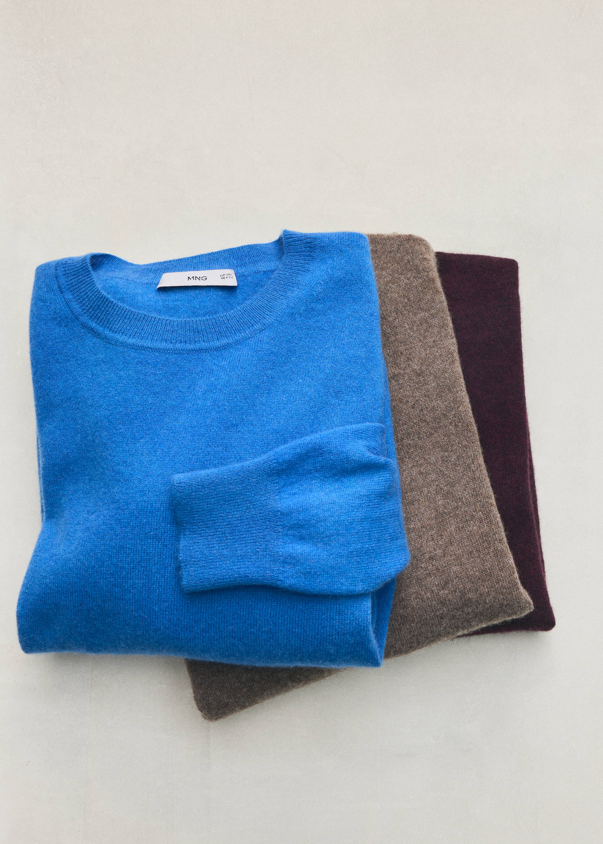 Folded bright blue crew-neck jersey stacked with brown and plum jerseys.