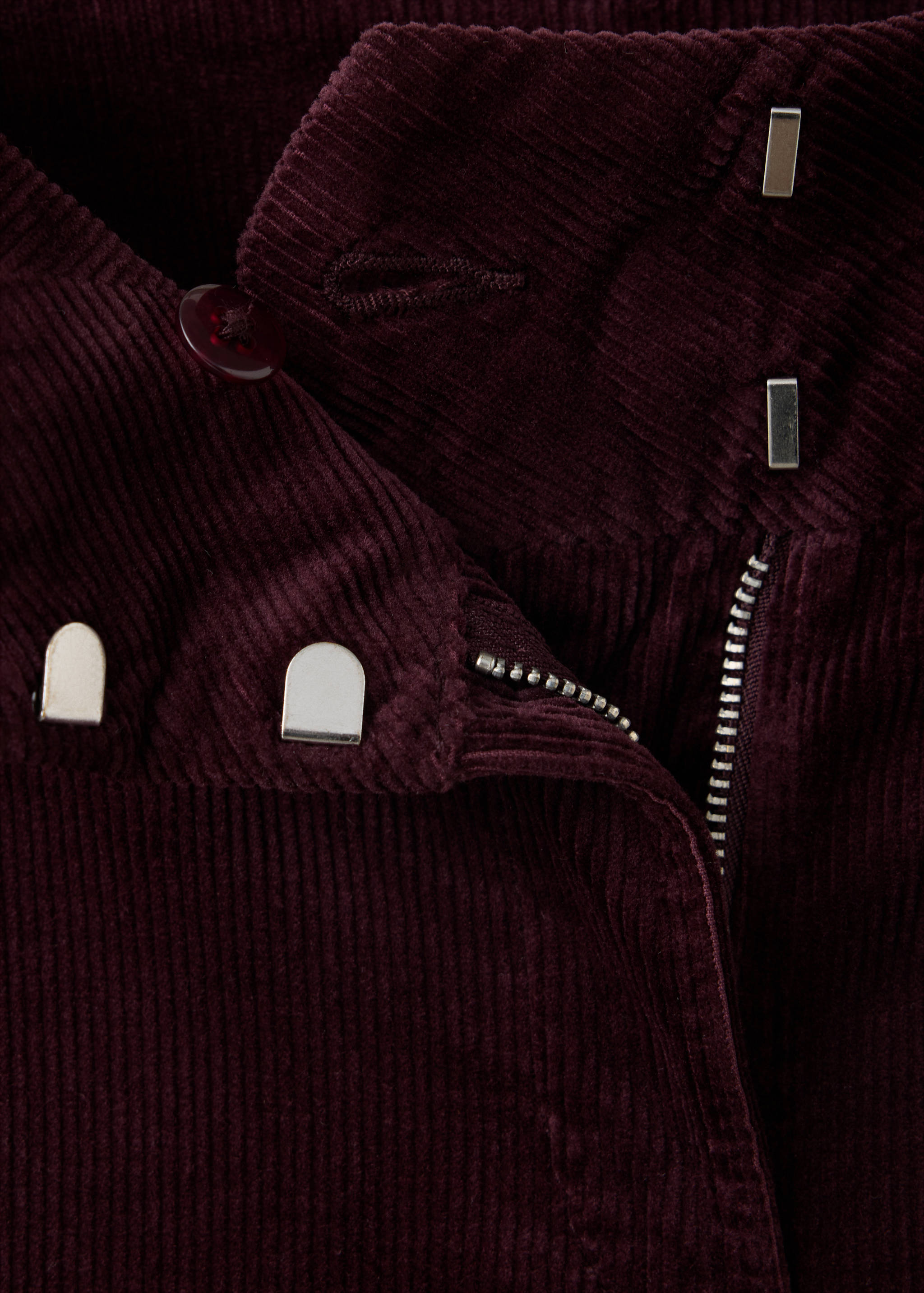 Close-up of deep burgundy corduroy trousers showing the waistband and zip detail.