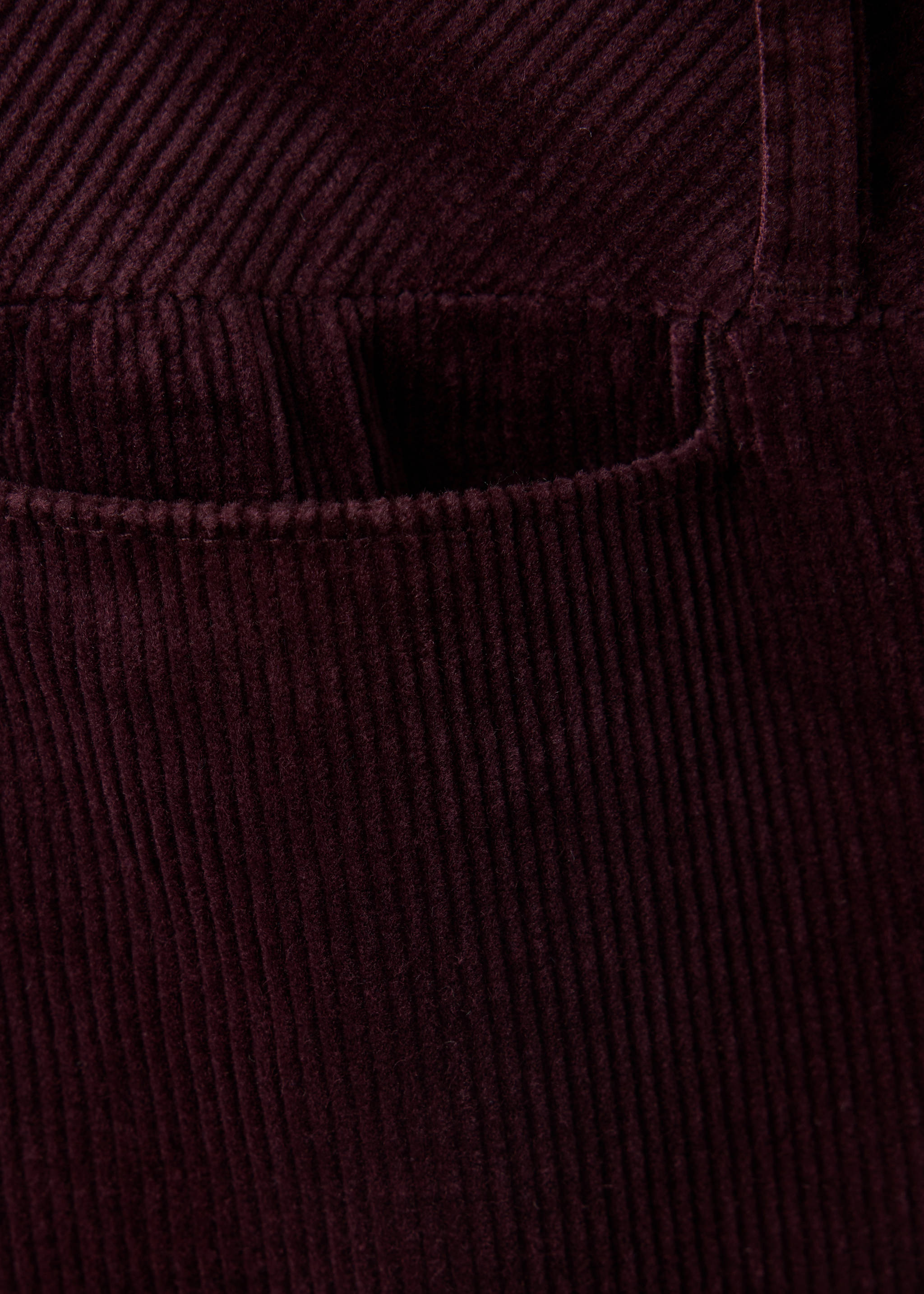 Burgundy corduroy trousers fabric detail showing texture and pocket.