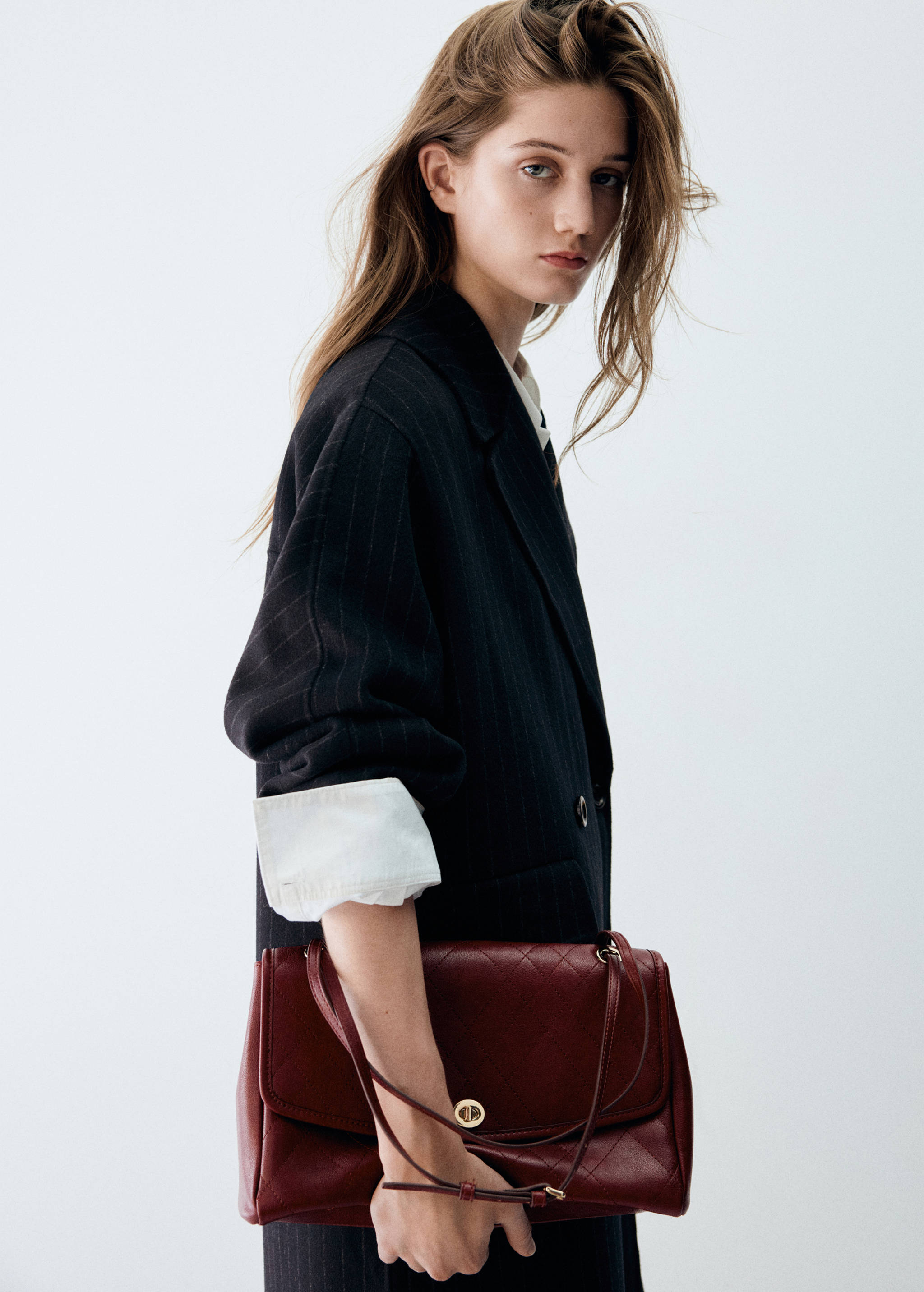 Close-up portrait in a dark grey pinstripe coat with a burgundy quilted bag.