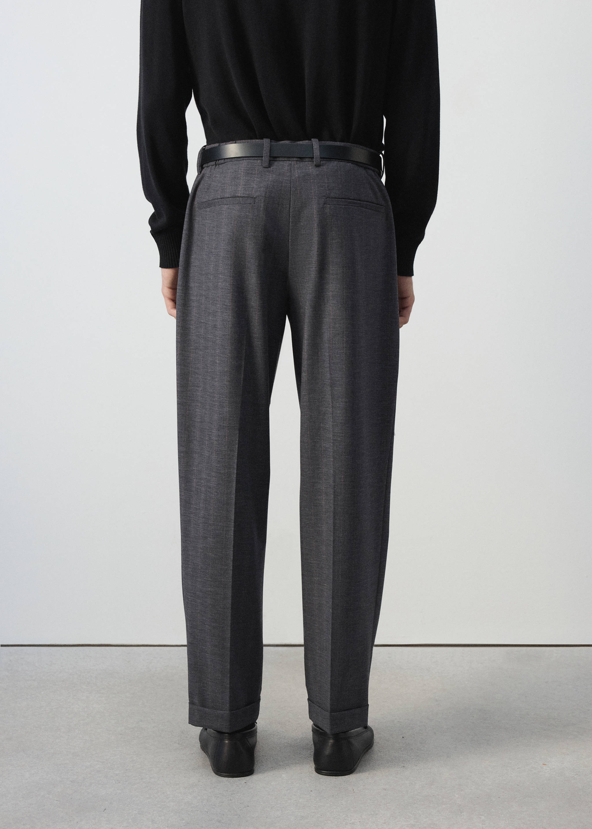 Pantalones de traje en gris oscuro vistos desde atrás, con cinturón, bolsillos traseros y bajos con vuelta.