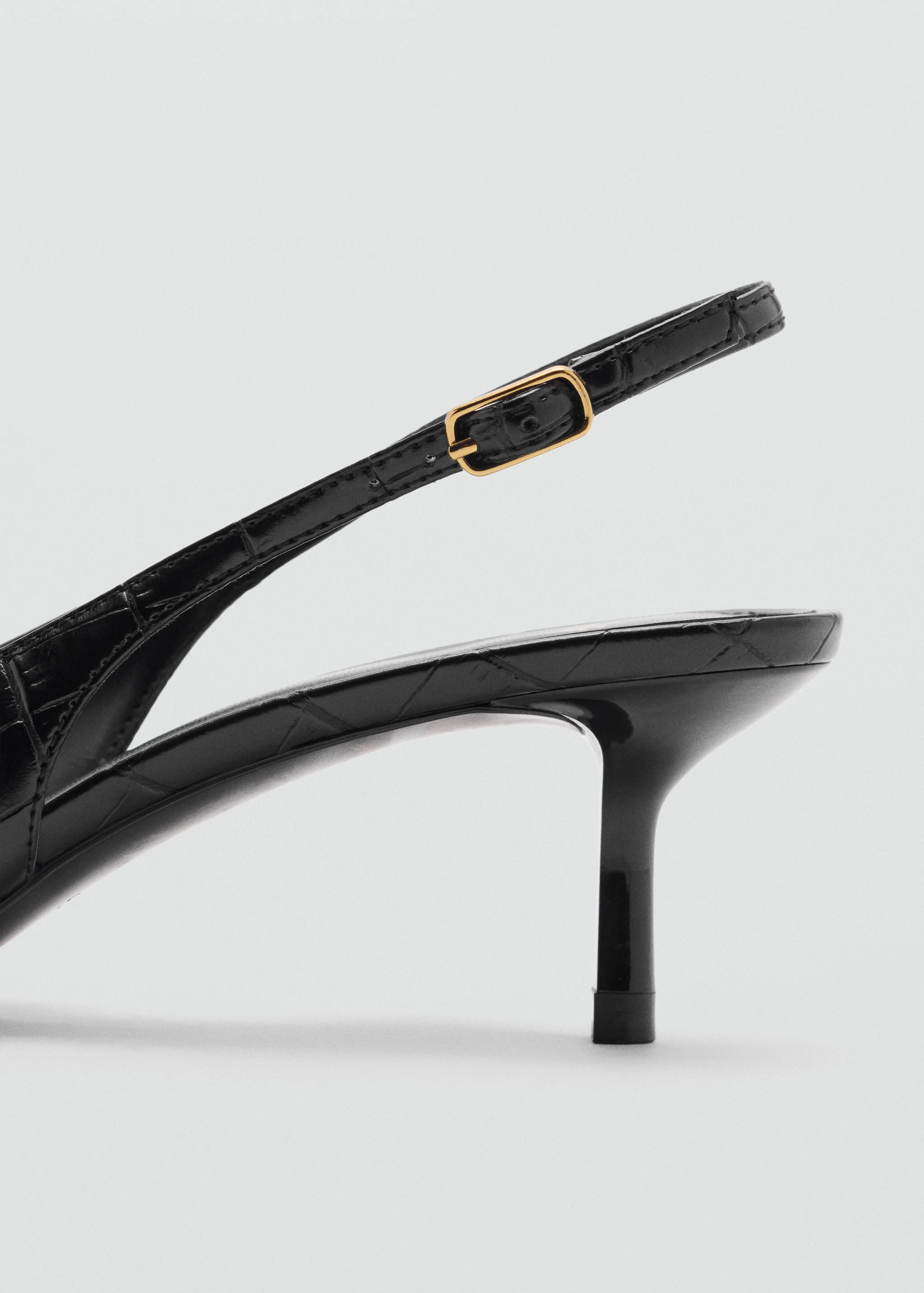 Black slingback shoe detail with a glossy embossed finish and a gold buckle.