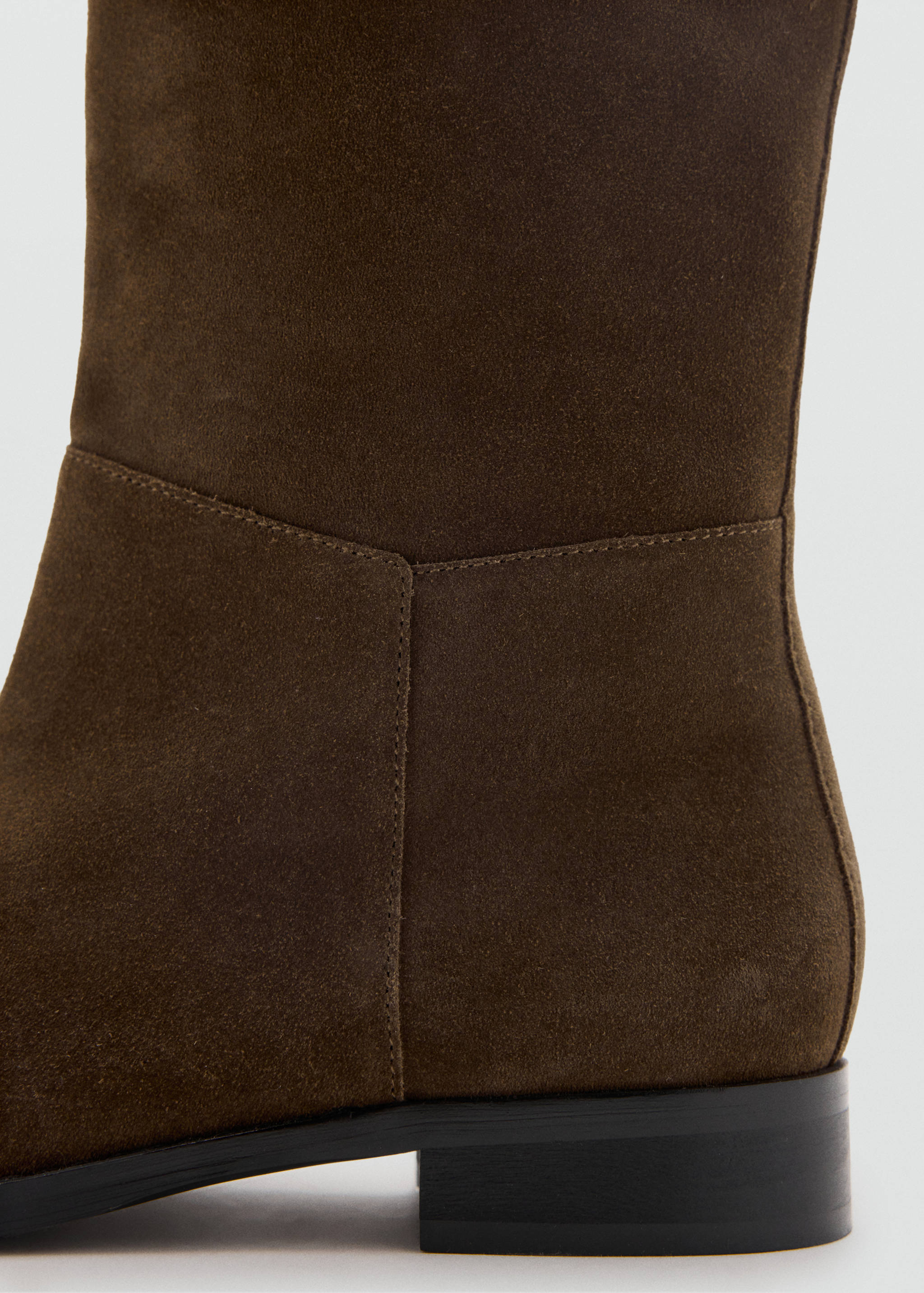 Close-up of a dark brown suede boot featuring tonal stitching and a low heel.