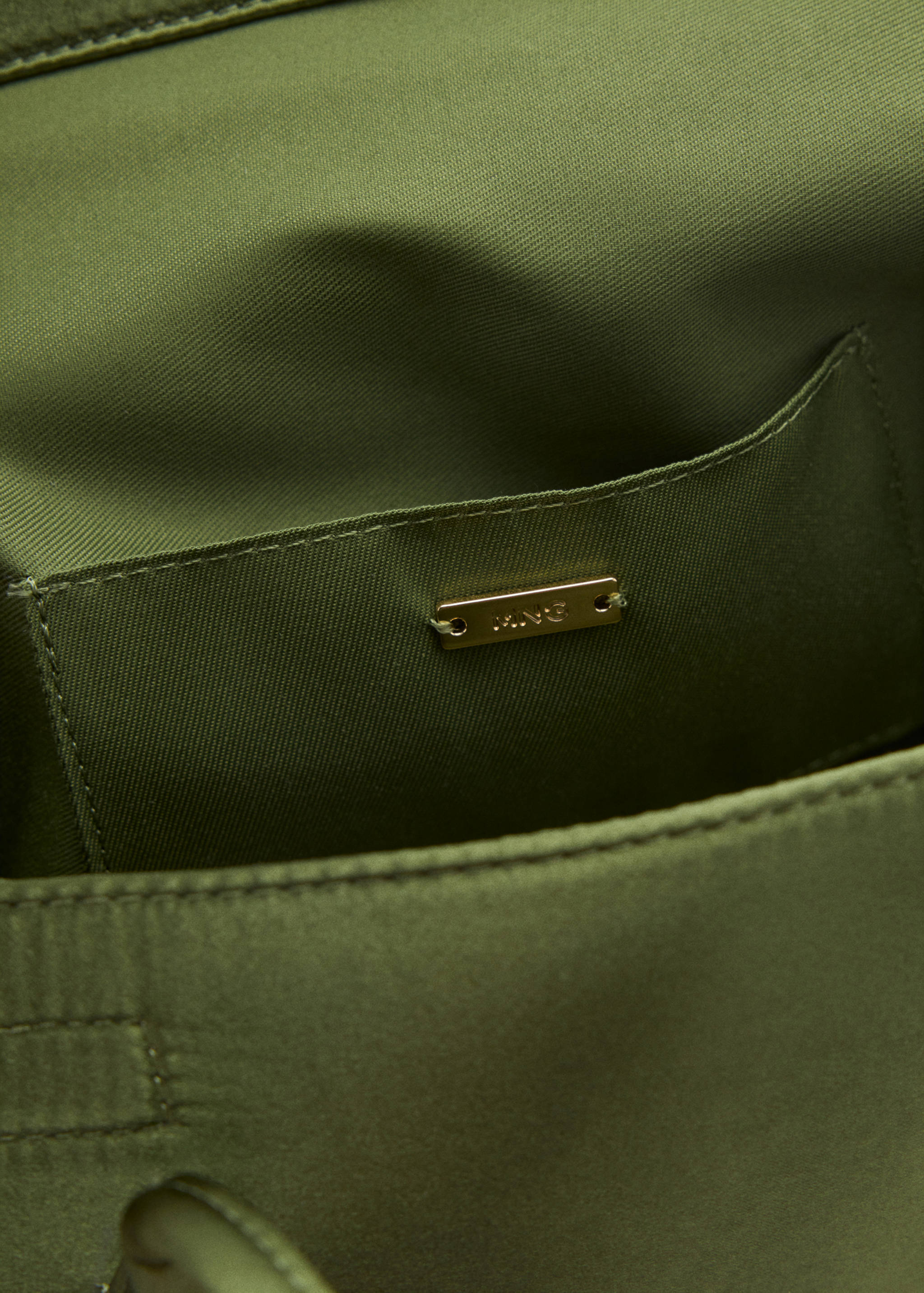 Close-up of an olive green shoulder bag interior showing the pocket and gold brand plaque.