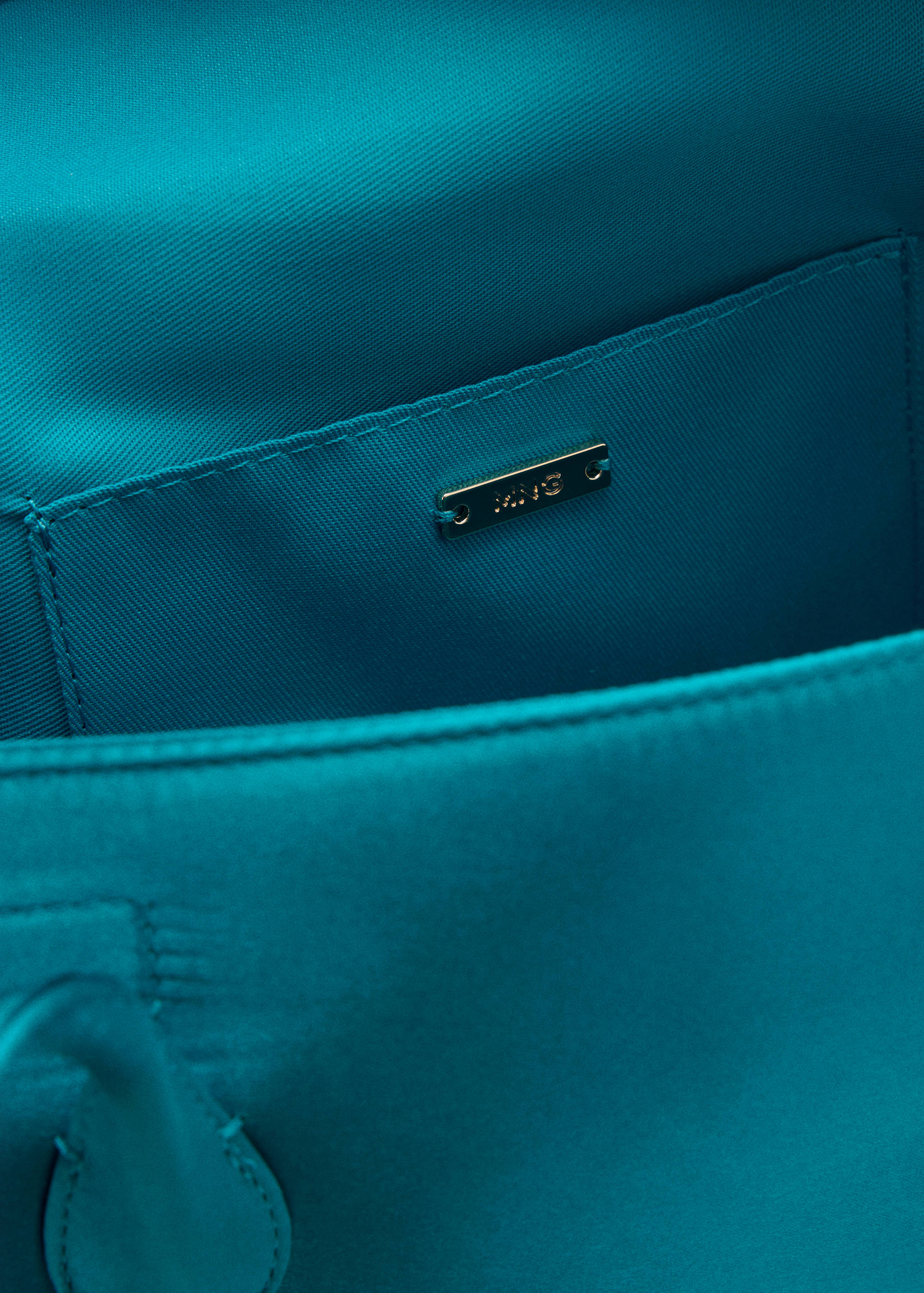 Close-up of the turquoise shoulder bag interior showing a slip pocket and gold-tone logo plaque.