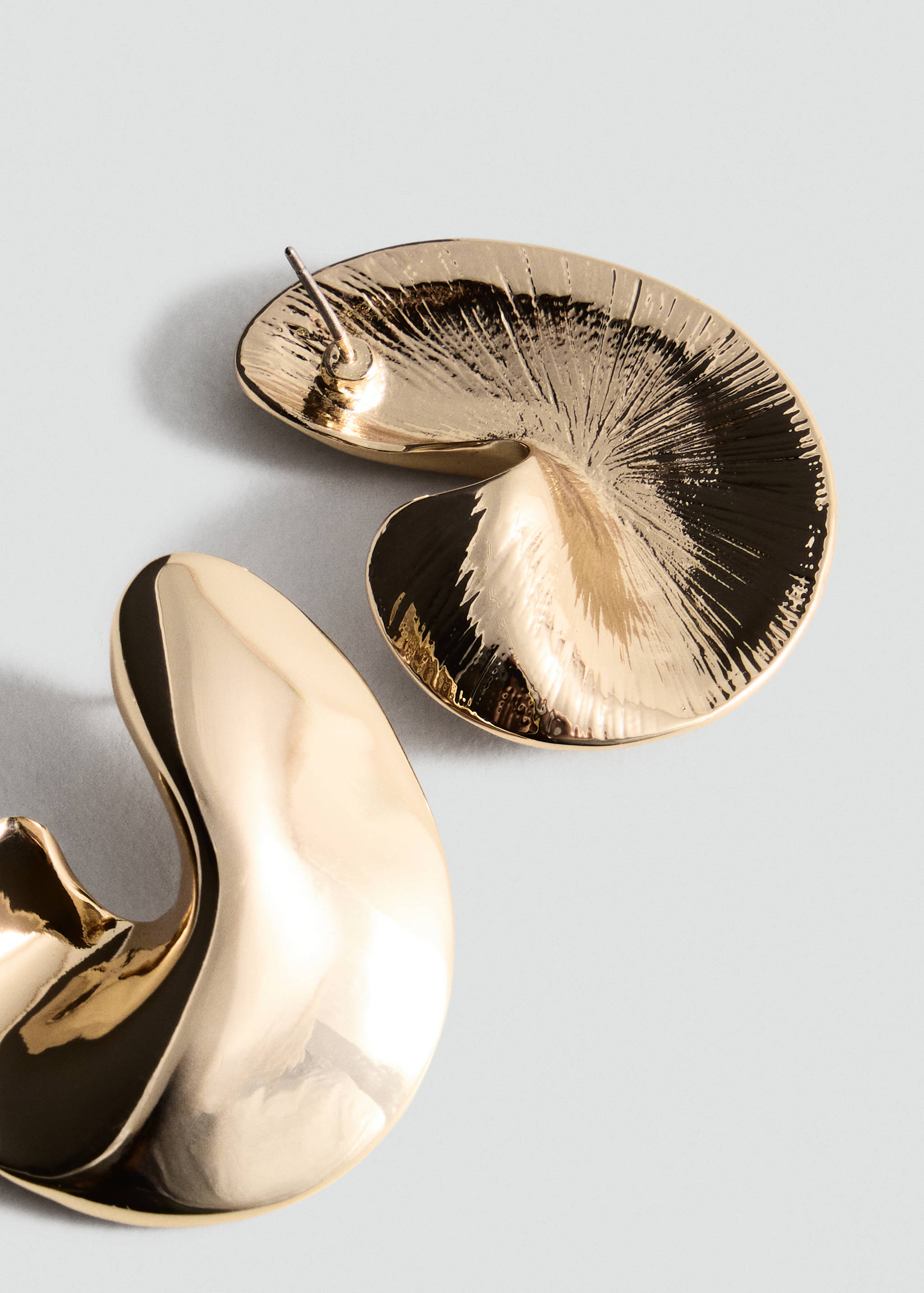 Close-up of sculptural gold-coloured metal earrings with an organic, polished finish.
