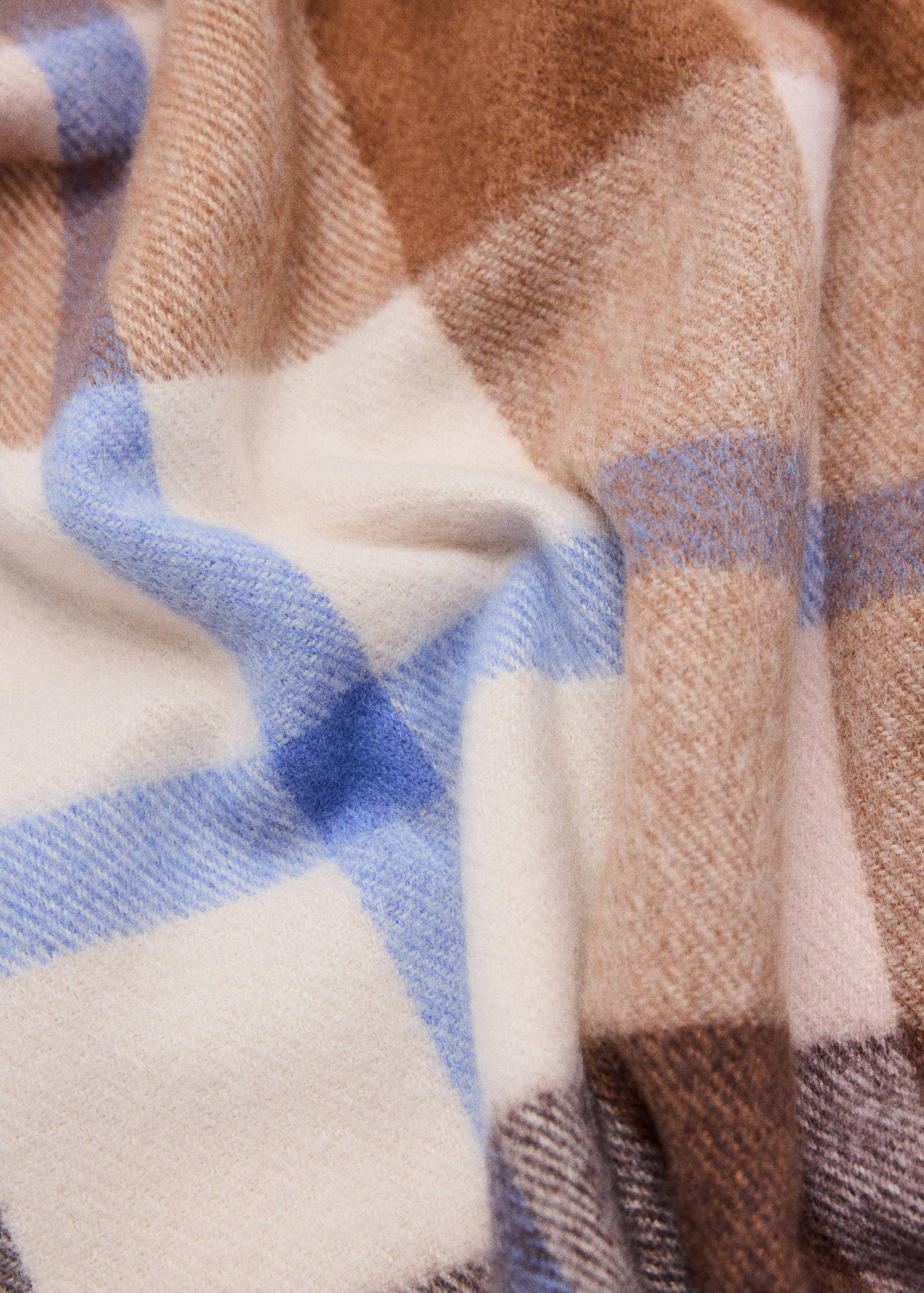 Close-up of a soft scarf with a brown, beige and blue plaid pattern.