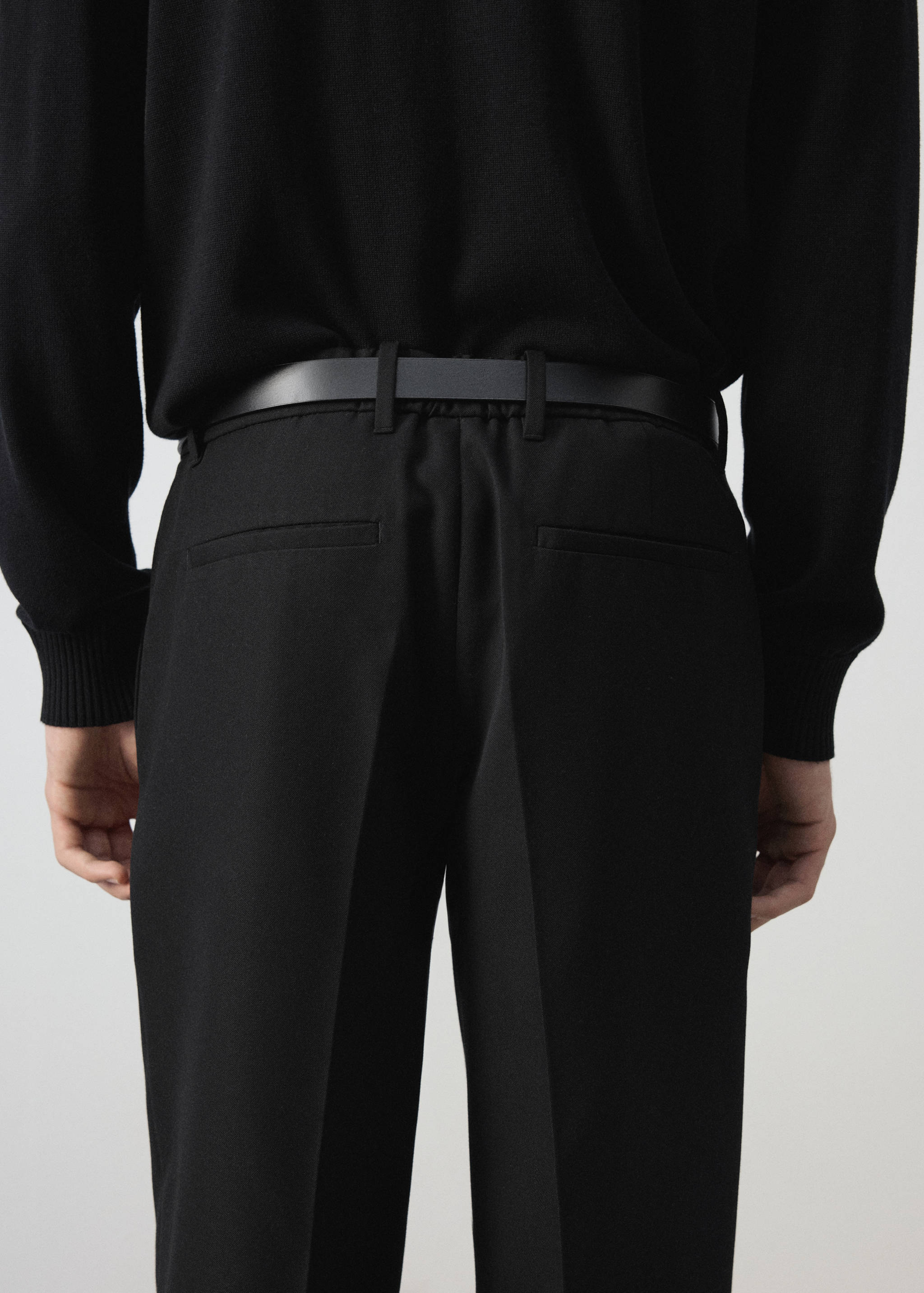 Vista trasera de unos pantalones negros con trabillas y bolsillos de vivo.