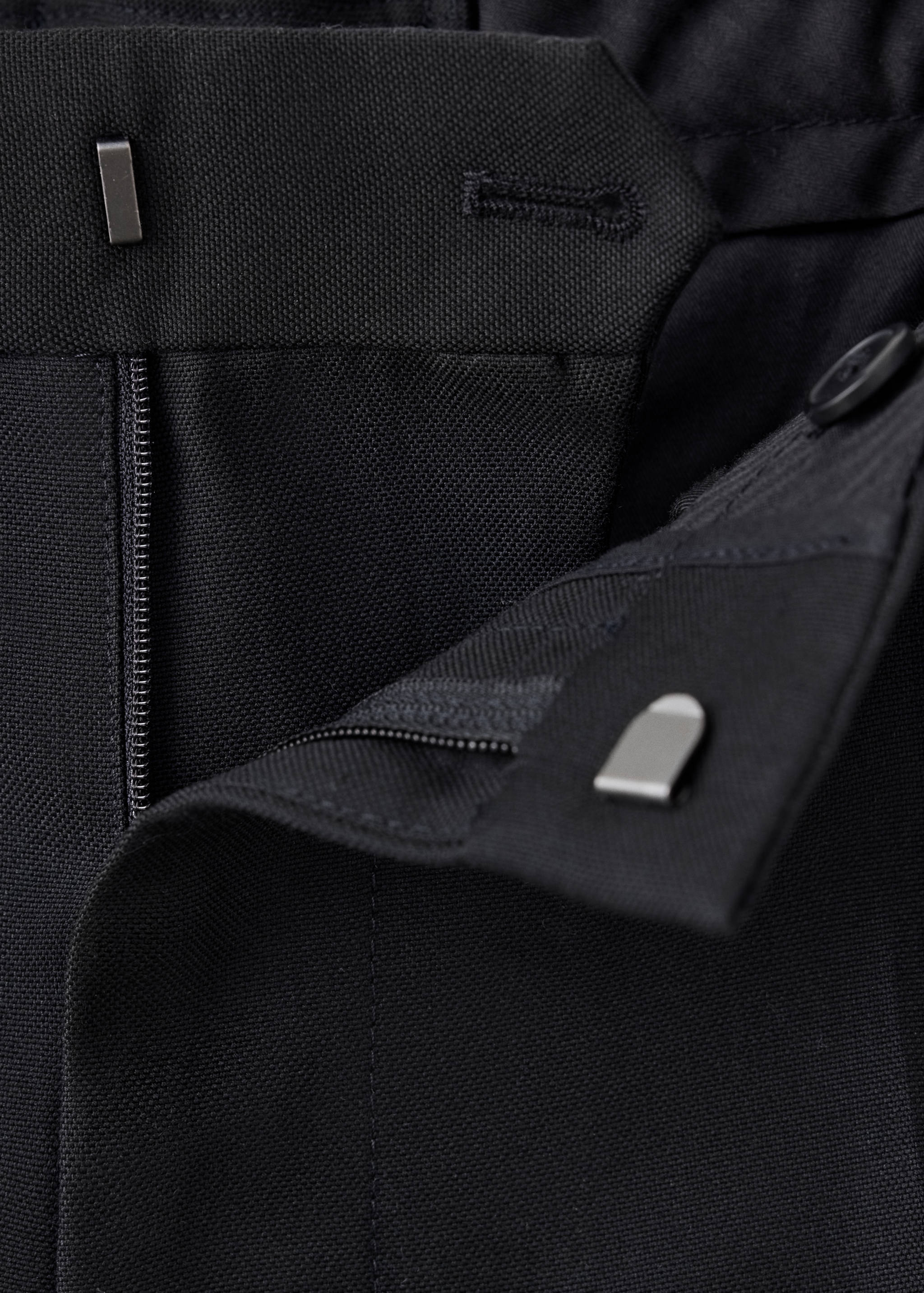 Detalle de pantalón negro que muestra la cinturilla, la cremallera y el cierre de botón.
