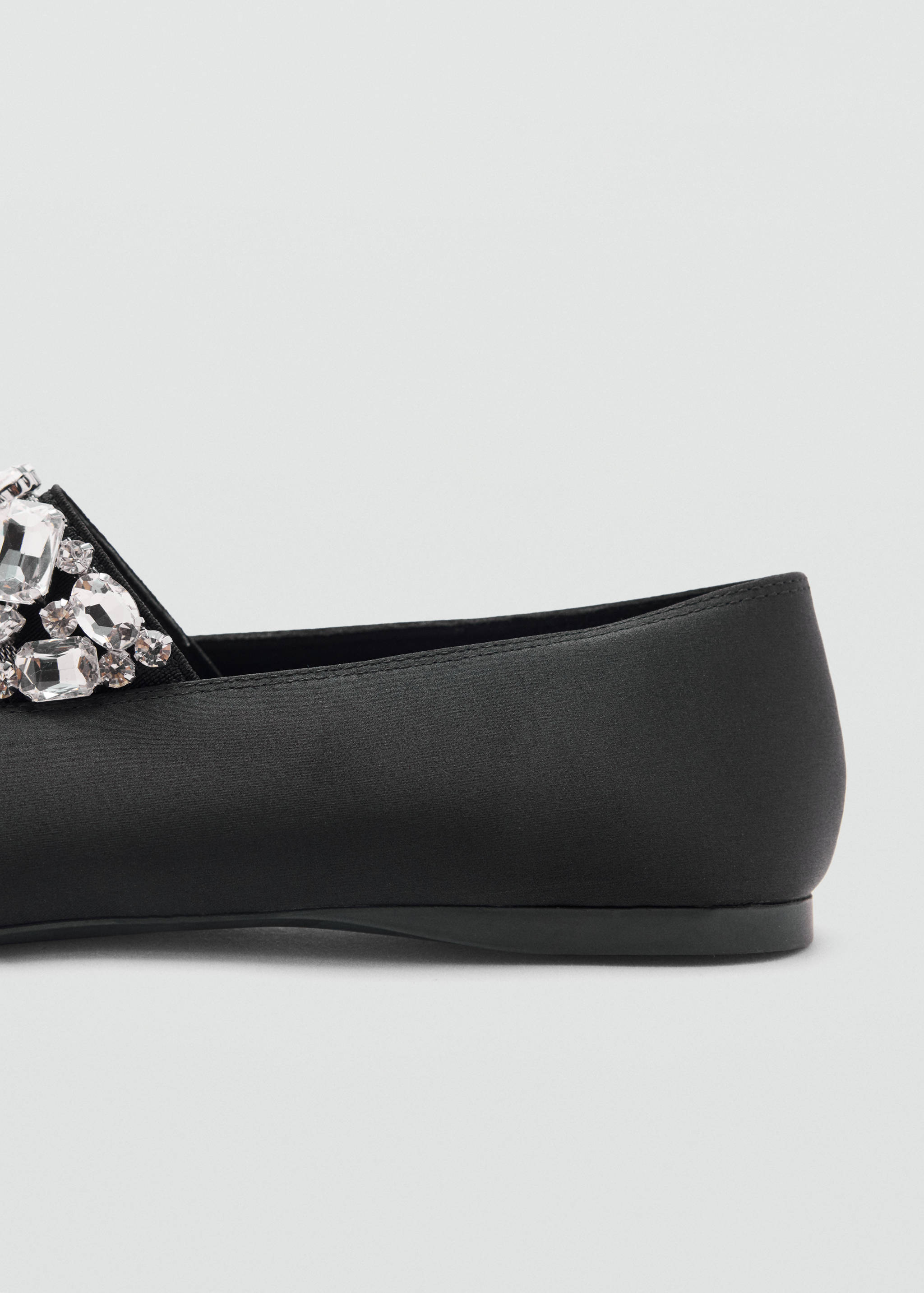 Close-up of a black satin shoe with a rhinestone-embellished toe.