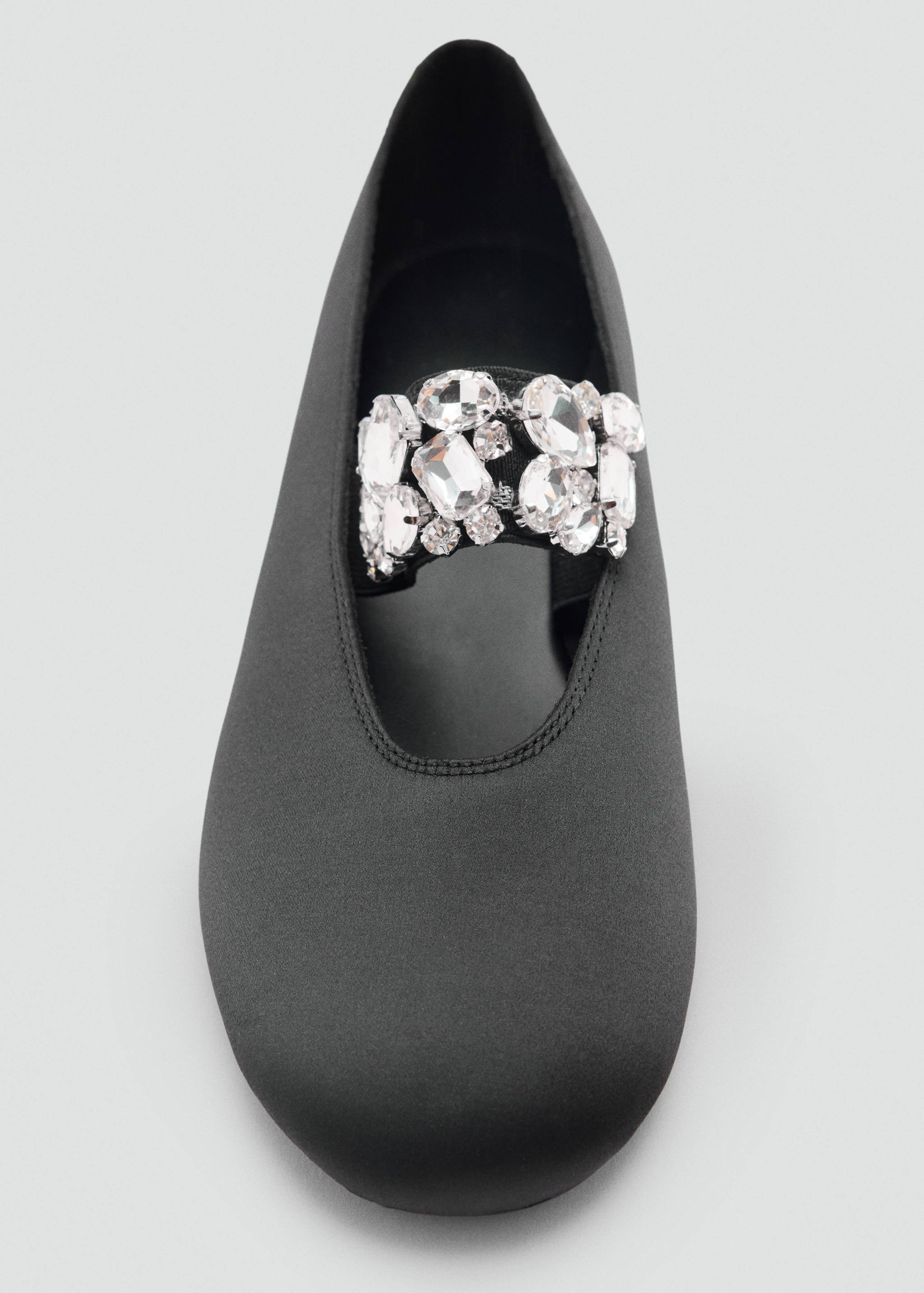Black flat shoe with a rounded toe and a rhinestone-embellished strap.