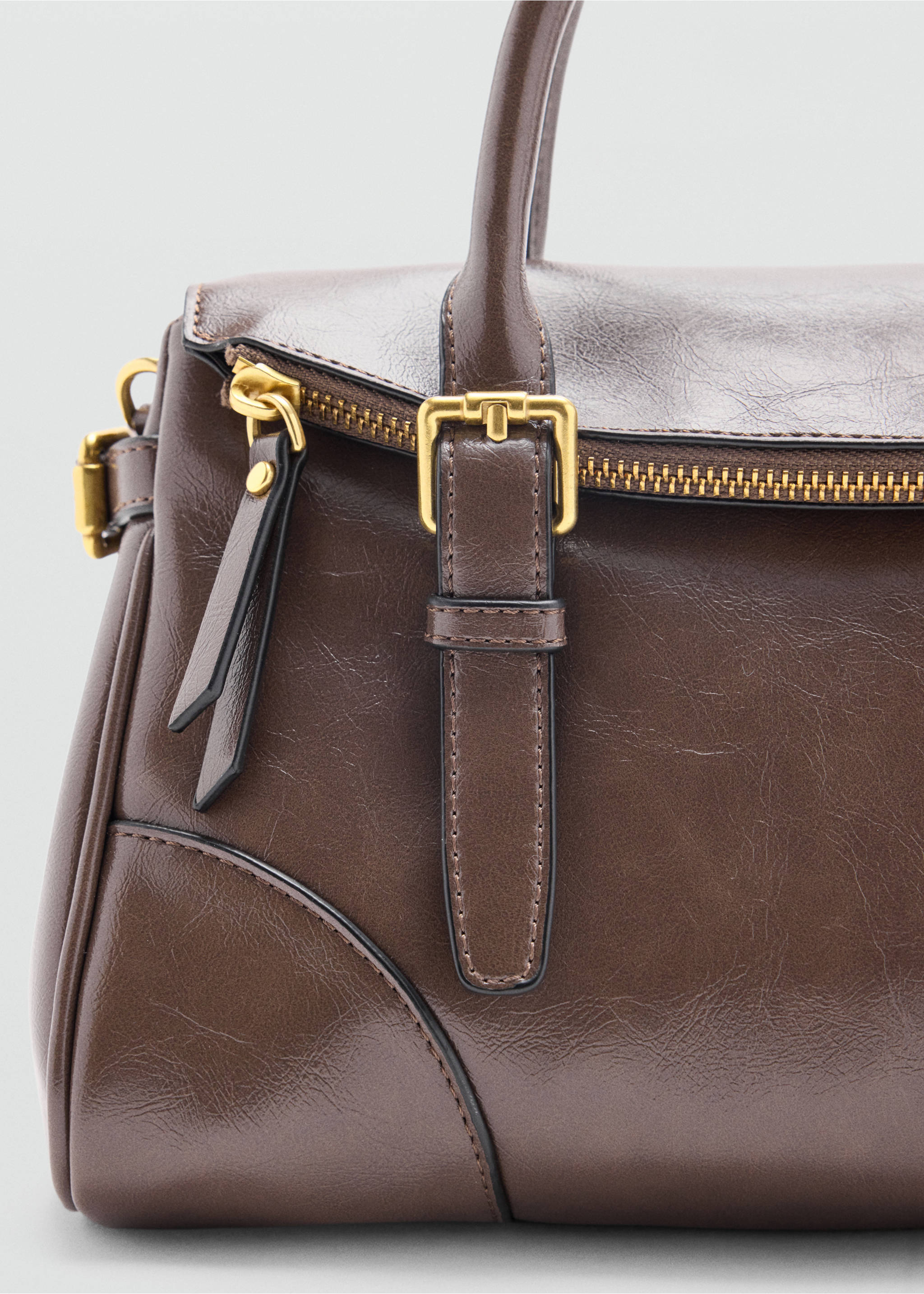 Close-up of a dark brown city bag with gold-tone hardware and buckle detail., Medium Brown. Ref: 47051345-00.