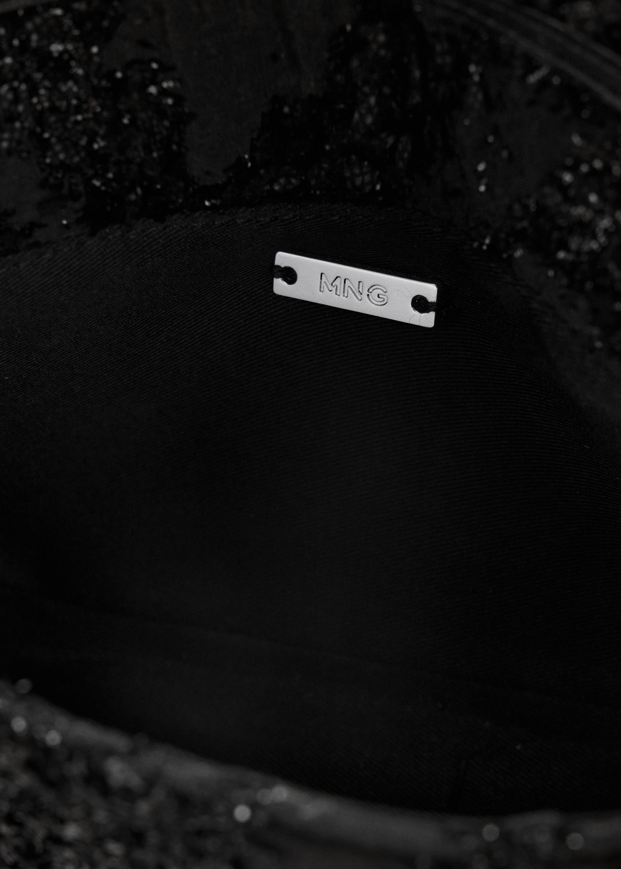 Close-up of a black bandolera bag interior showing the silver MNG metal plaque.