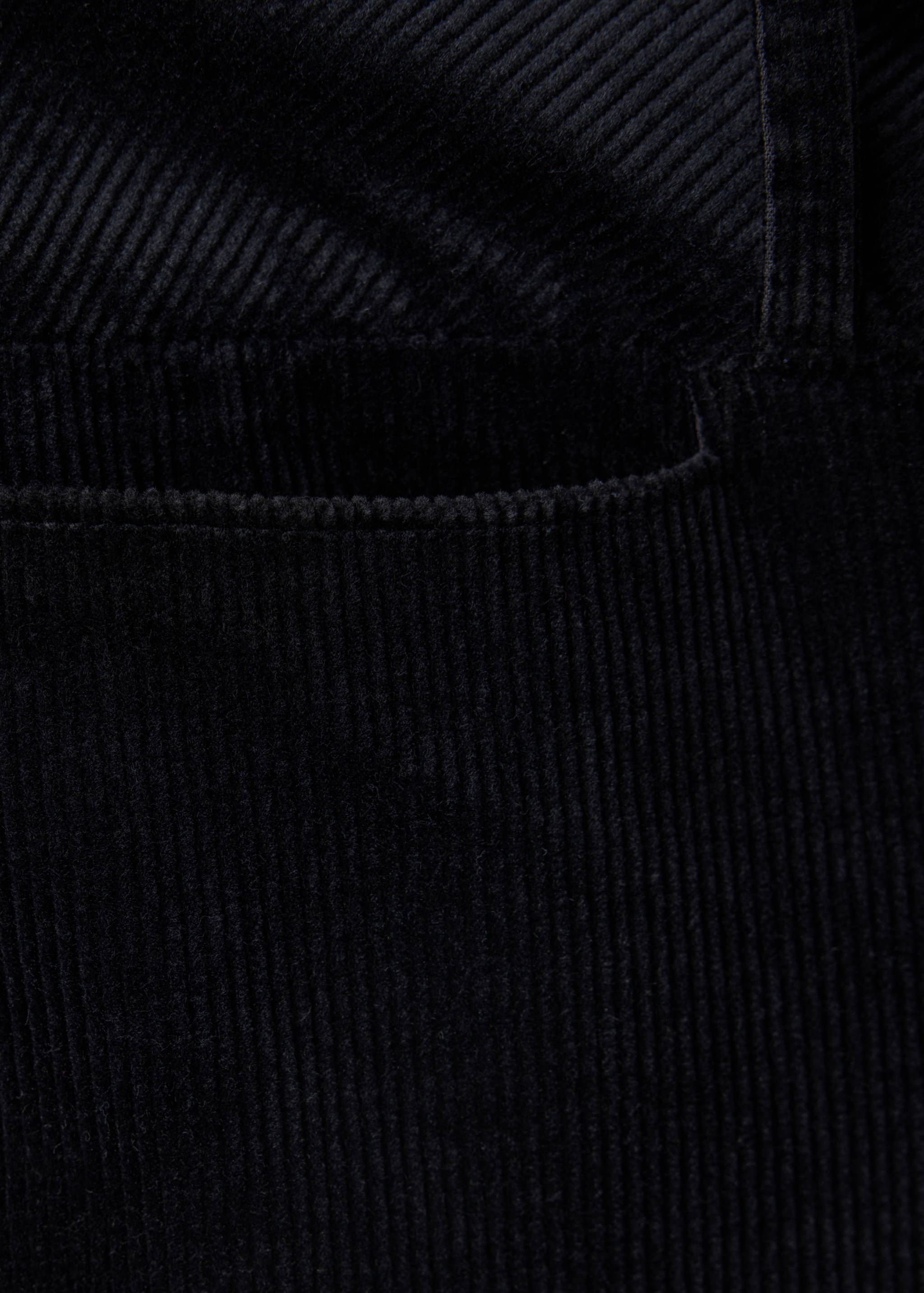 Black corduroy trousers detail showing fabric texture and pocket.