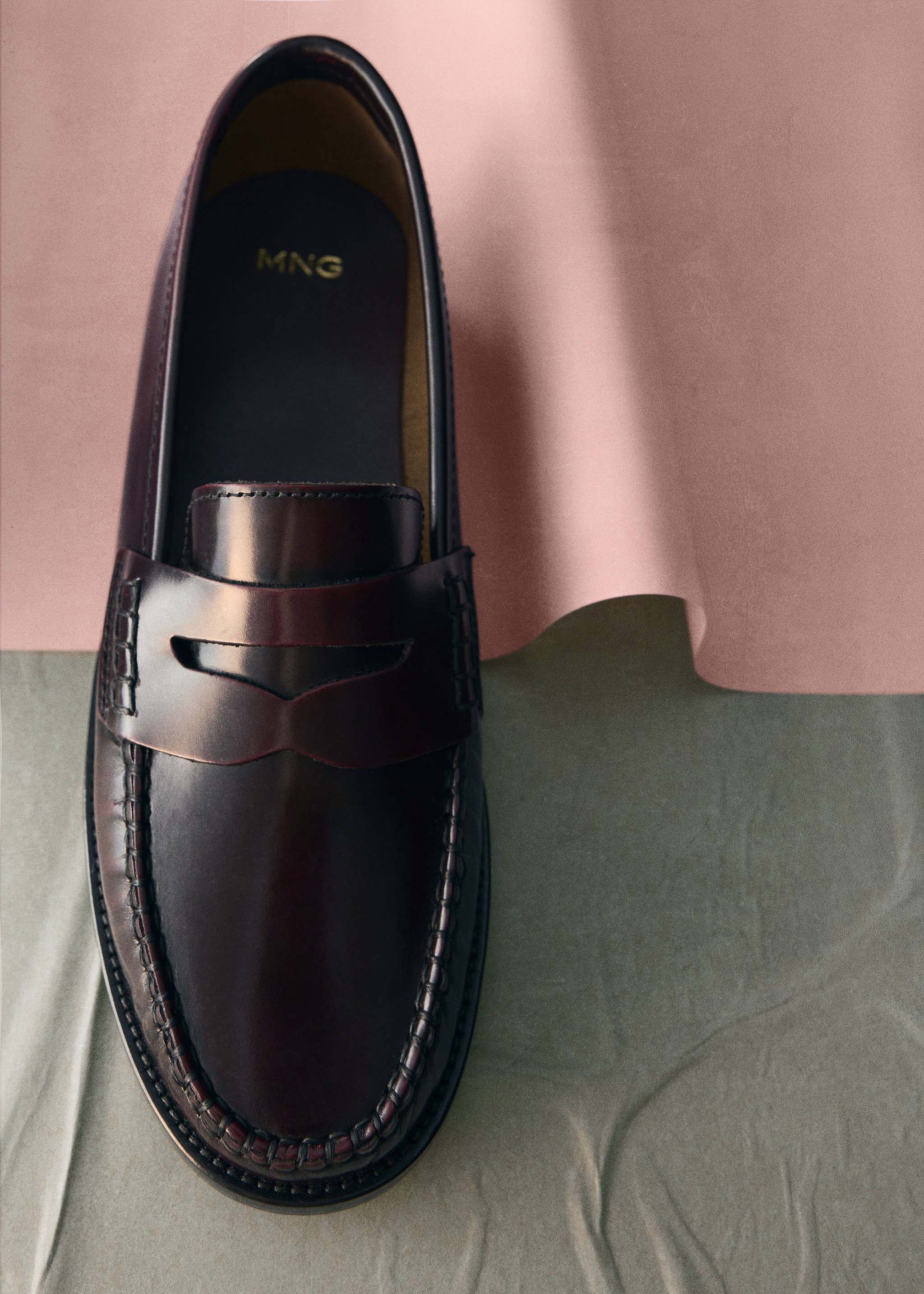 Dark burgundy leather penny loafer shoe on a textured surface.