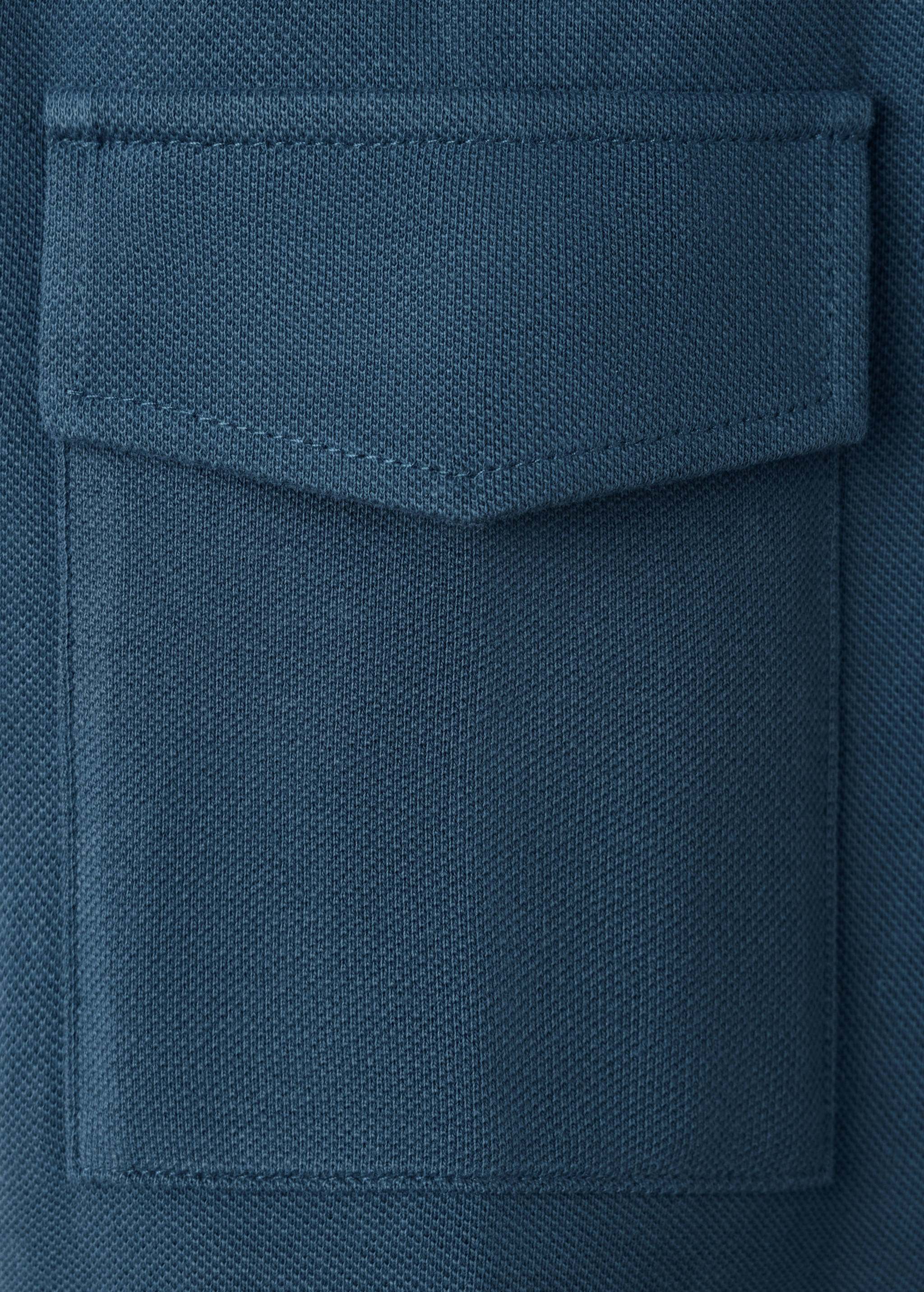 Close-up of blue polo shirt fabric showing textured knit and chest pocket.