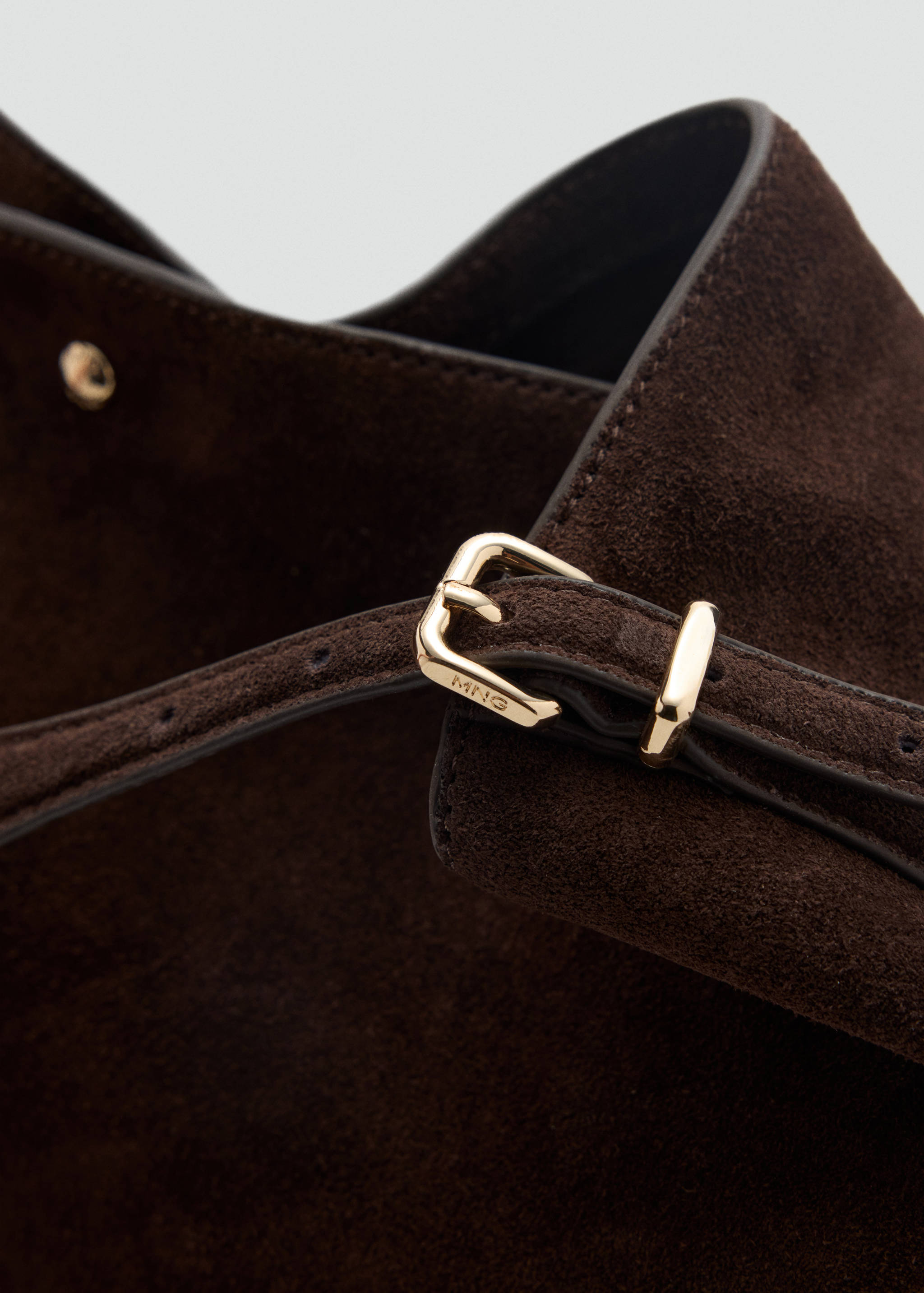 Close-up of a dark brown suede bucket bag with gold-toned hardware.