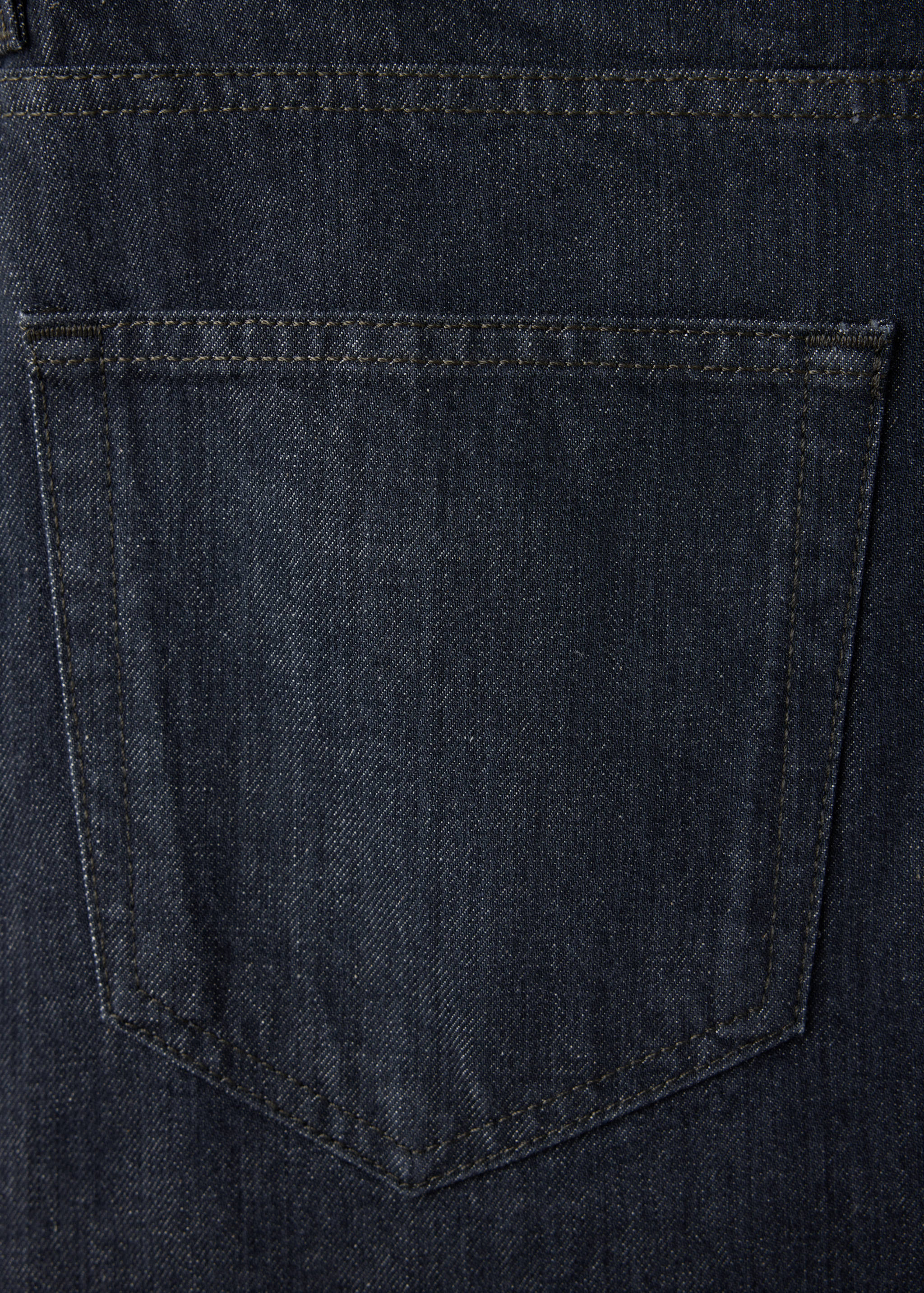 Close-up of dark blue denim fabric and back pocket detail on men's trousers.