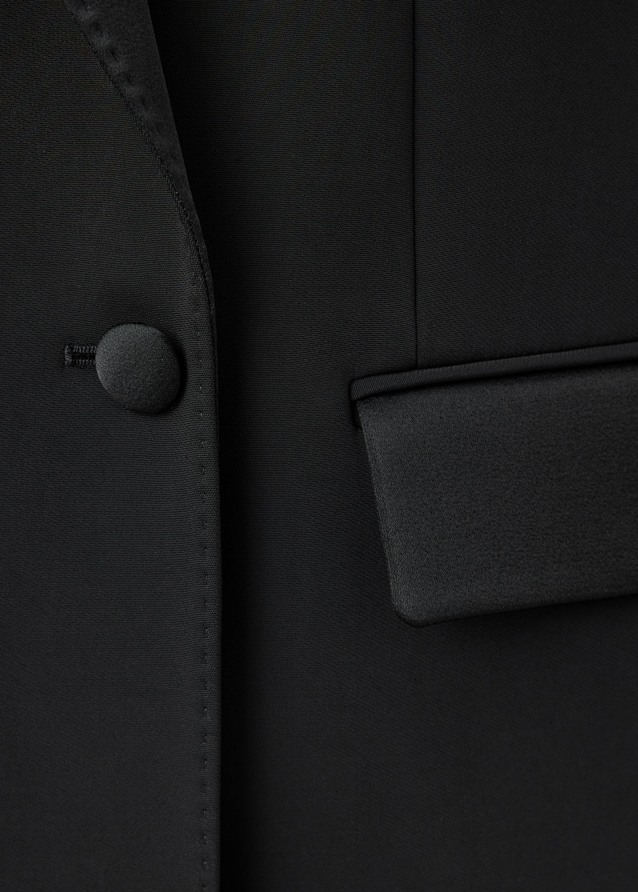 Black blazer detail with a satin button and pocket flap.