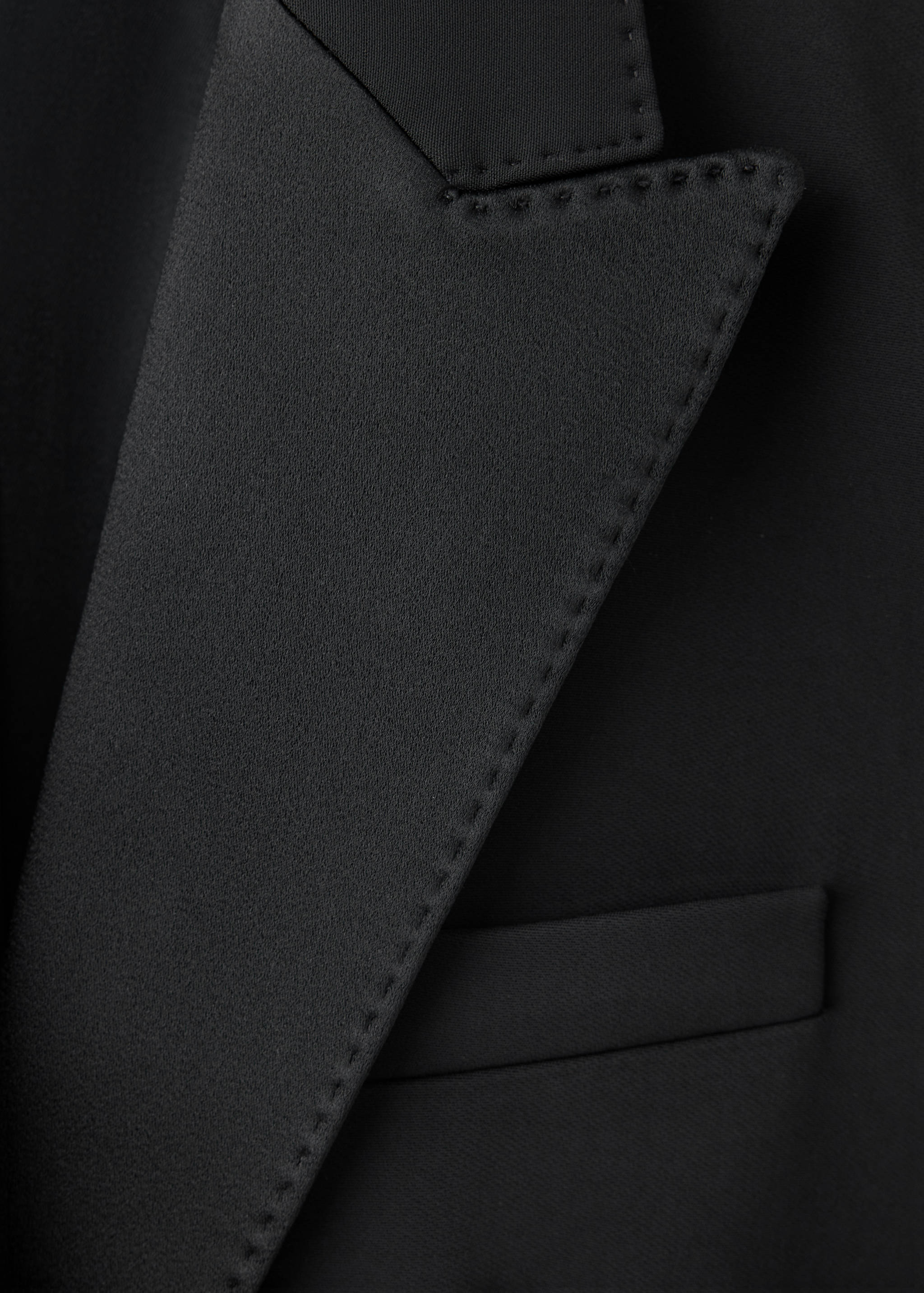 Close-up of a black blazer showing the satin peak lapel and topstitching detail.