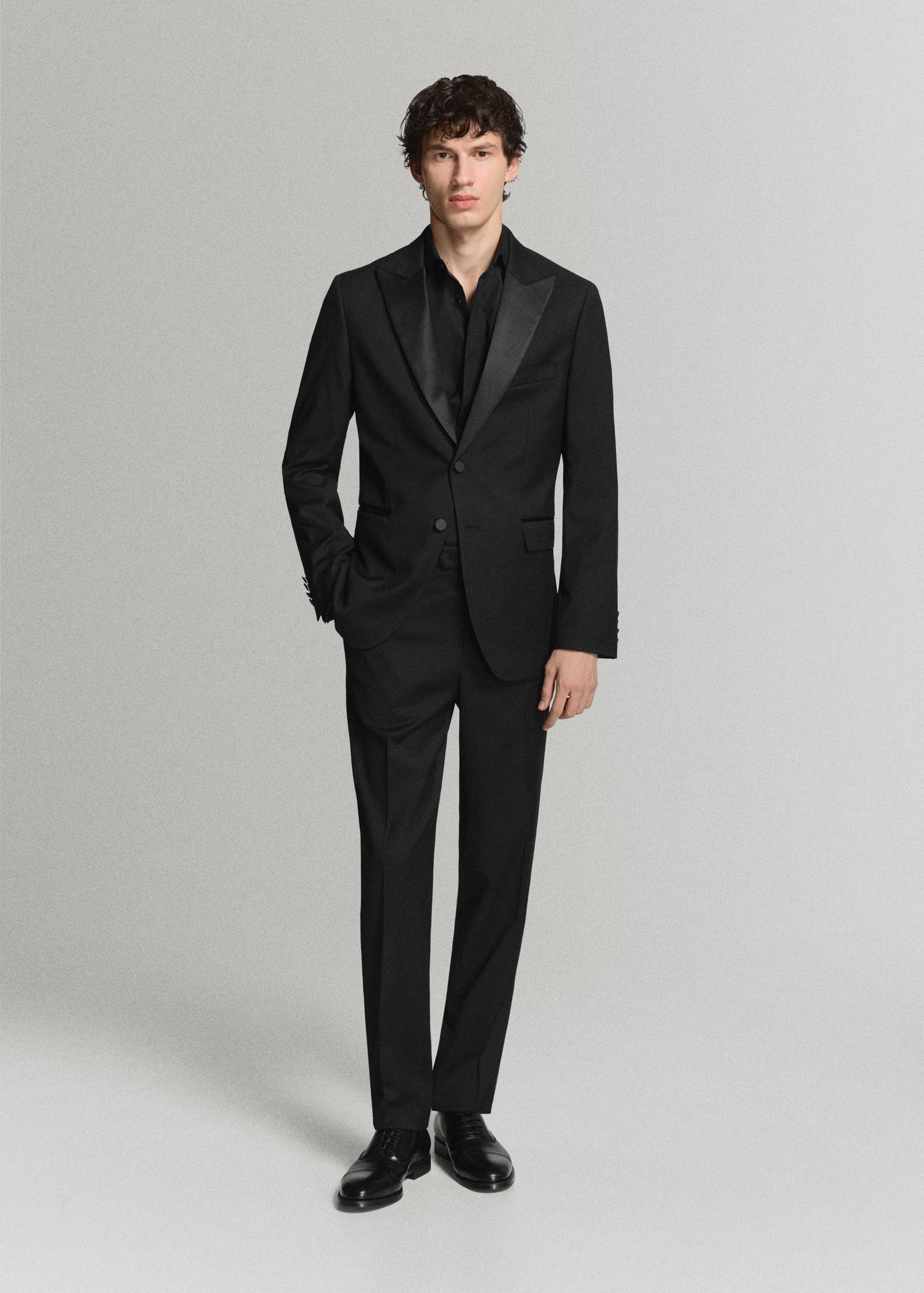Black shirt worn under a tailored black suit with satin lapels
