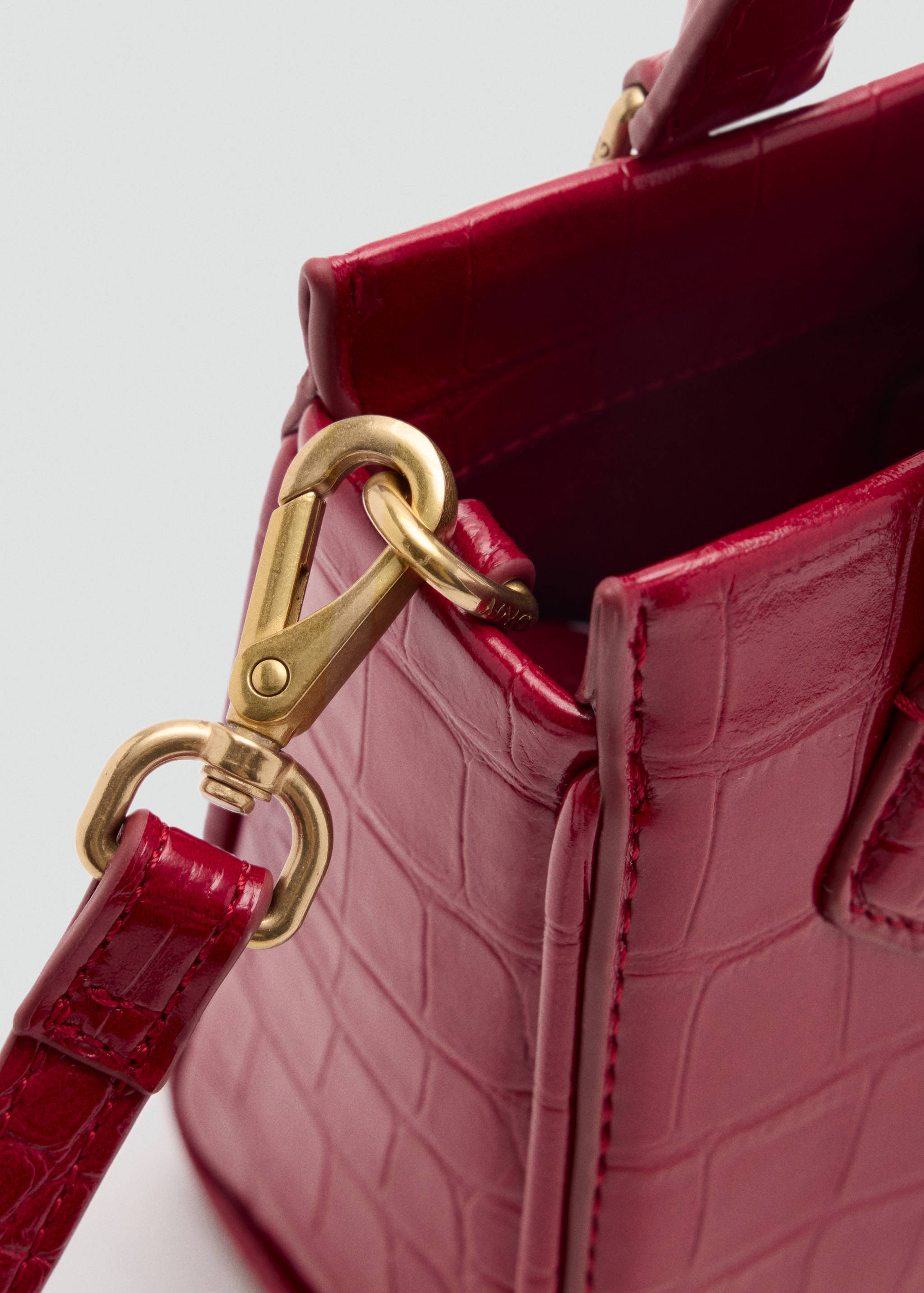 Close-up of a red crocodile-effect cross-body bag featuring gold-tone hardware details.