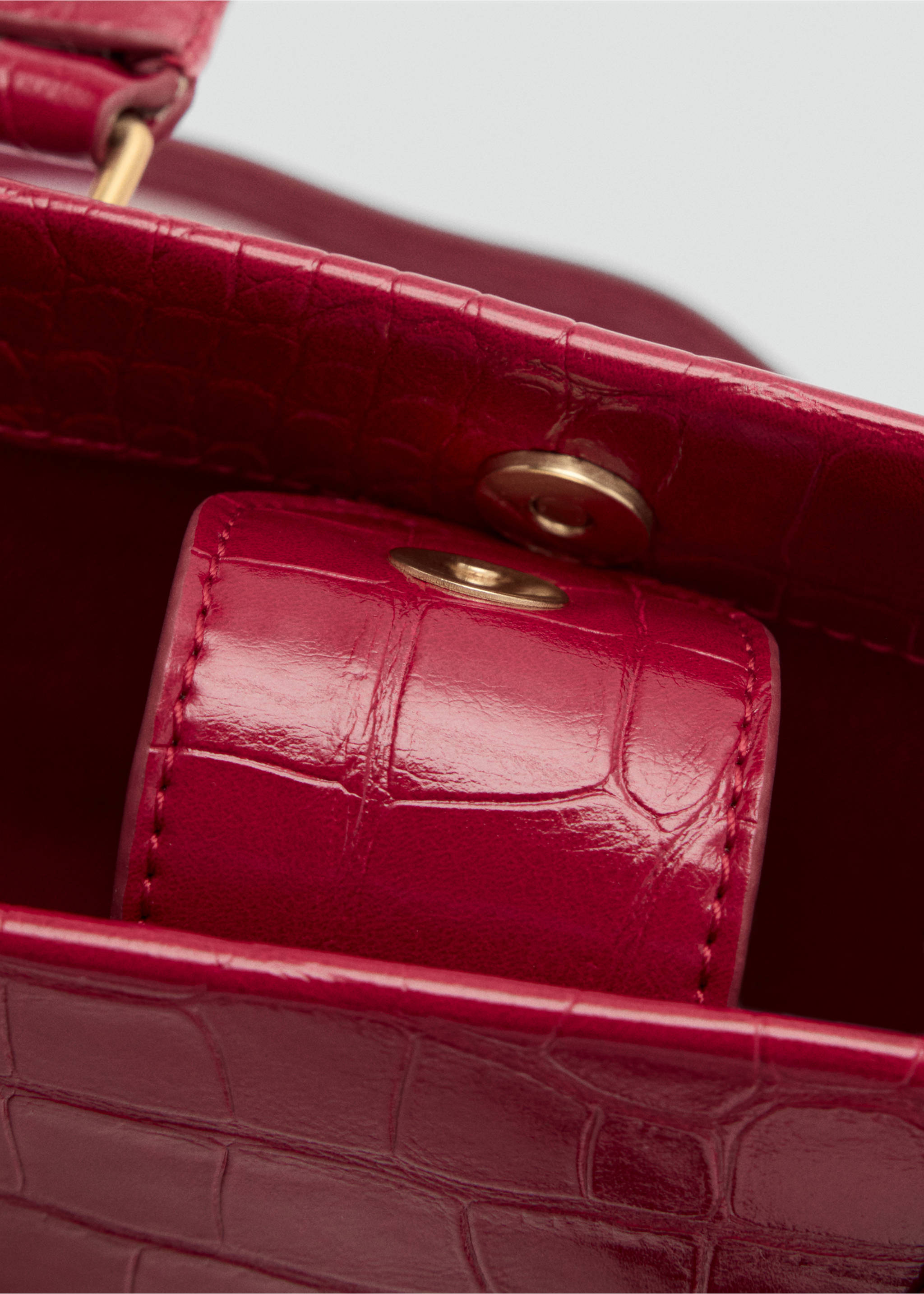 Close-up of the magnetic closure on a magenta faux-croc crossbody bag., Red. Ref: 47071340-00.