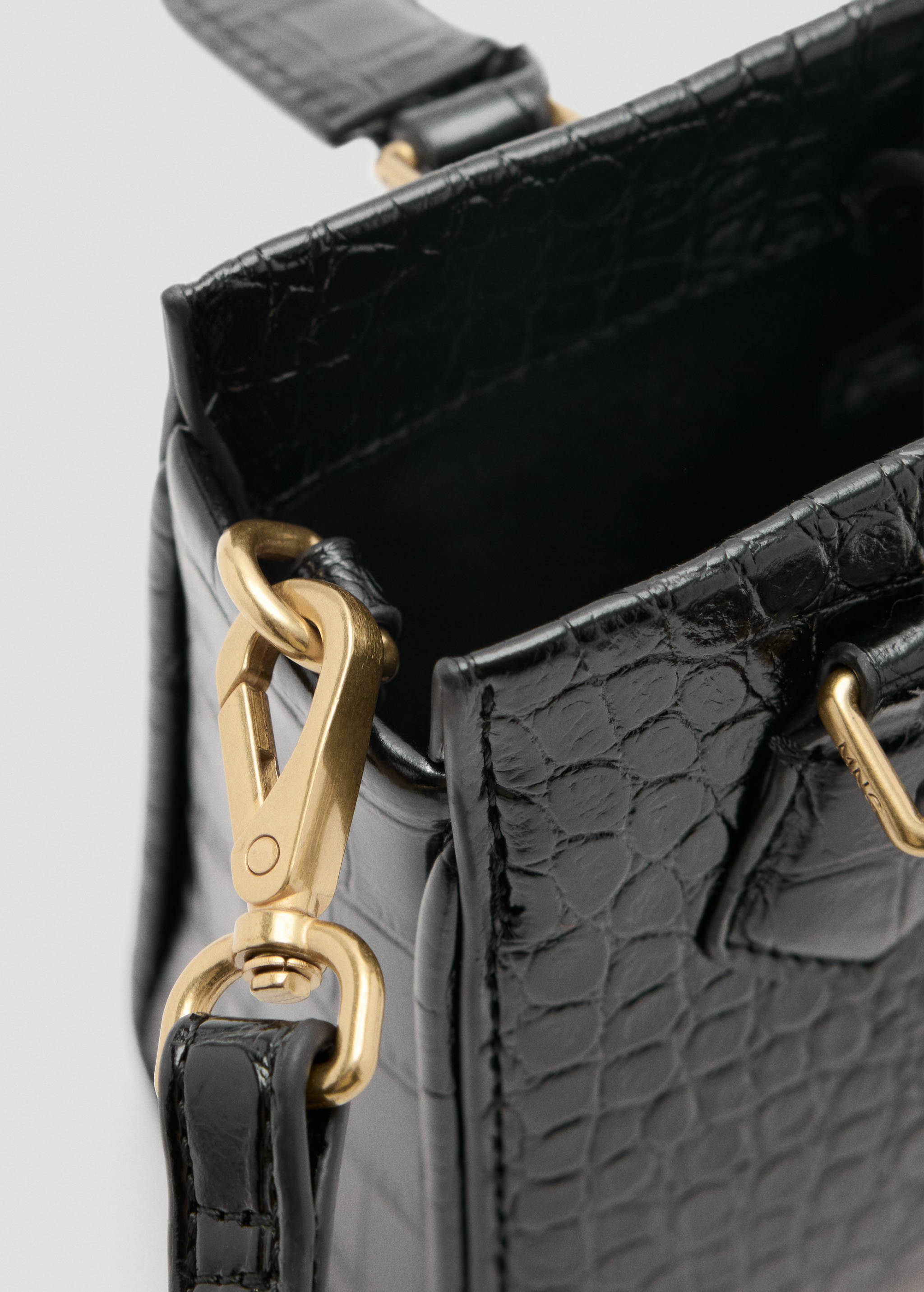 Close-up of a black croc-embossed crossbody bag with gold-tone hardware.